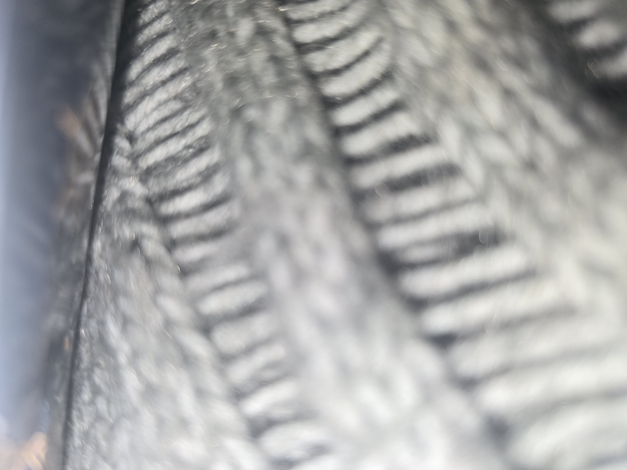 The image is a close-up, out-of-focus shot of a textured material, likely fabric, with alternating dark and light ribbed patterns. The lighting creates bokeh effects, appearing as blurred circular highlights. The dark areas are a deep gray or black, while the lighter areas are a bright white or light gray. The texture suggests a knitted or woven material, possibly wool or a synthetic blend. The overall impression is of a soft, tactile surface. There is no discernible location in Ulan-Ude, Russia, as the image lacks any recognizable landmarks or environmental context.
