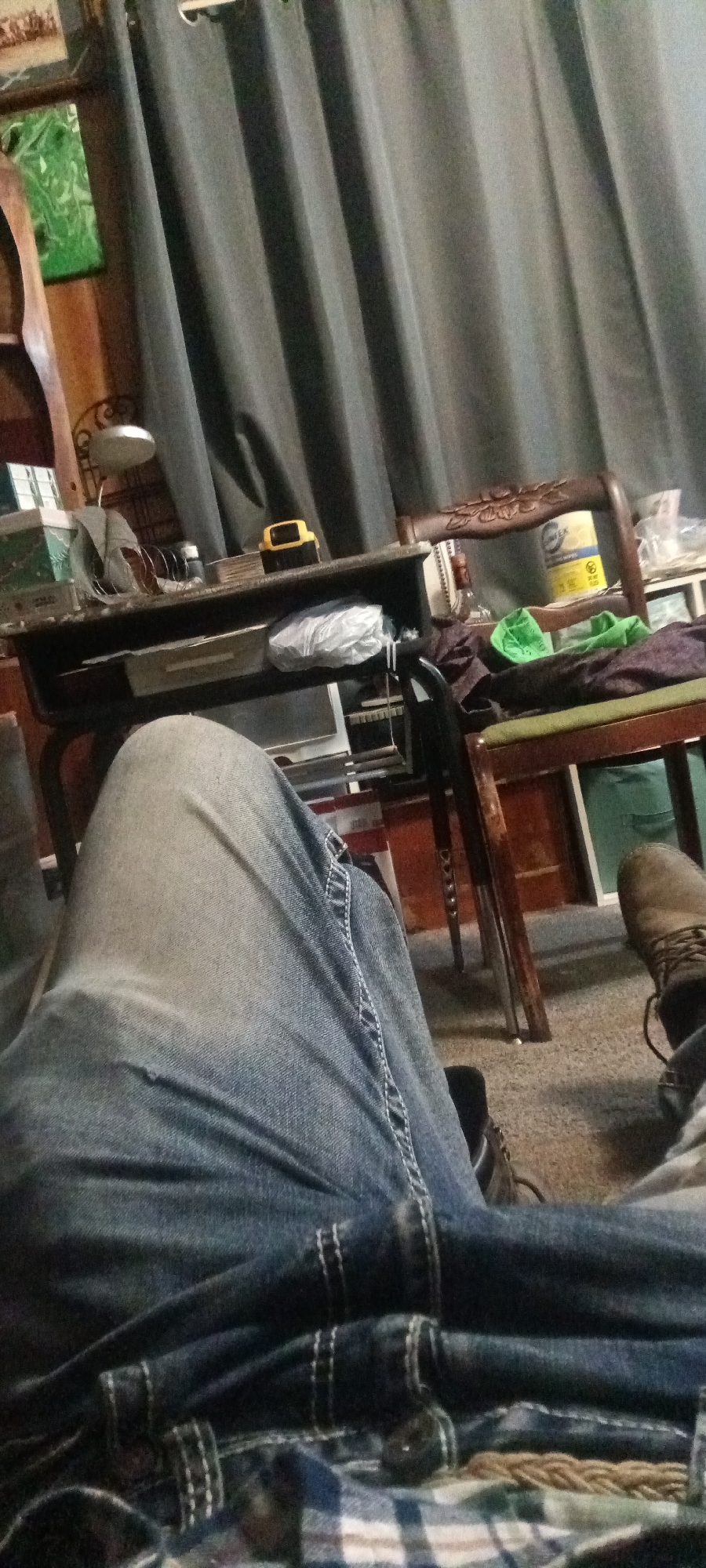 The image depicts a person's legs, clad in blue jeans, resting on a plaid fabric. The scene appears to be indoors, with a desk and chairs visible in the background. On the desk, there are various items including a lamp, a yellow object, and some containers. Dark gray curtains hang in the background, suggesting a window or alcove. The overall impression is of a casual, domestic setting. The location is specified as Coal Hill, United States of America.