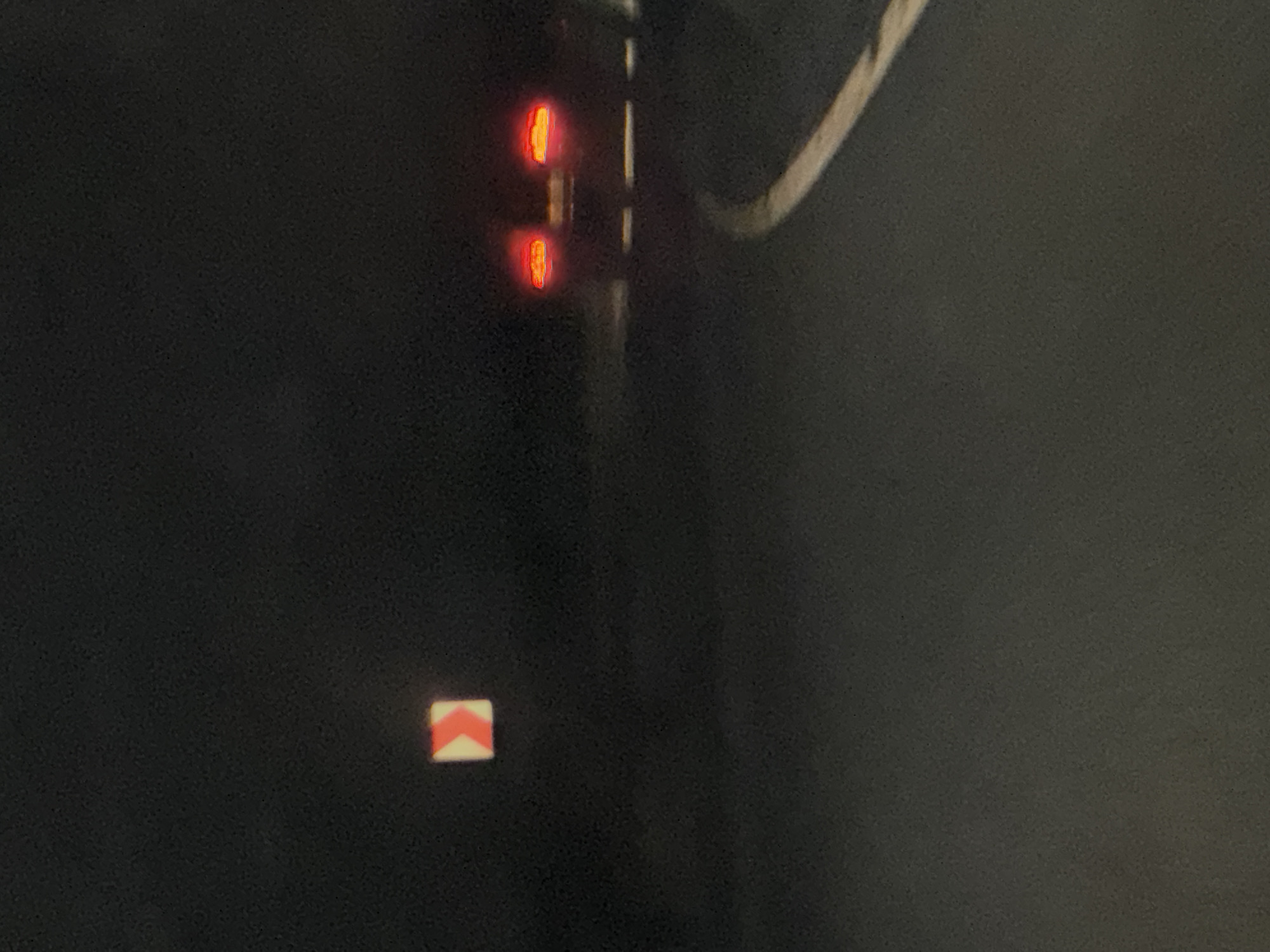 A night scene shows a vertical pole with two red lights at the top and a directional sign near the bottom. The sign is a white square with two red arrows pointing to the left. The setting appears to be Narechen, Bulgaria.