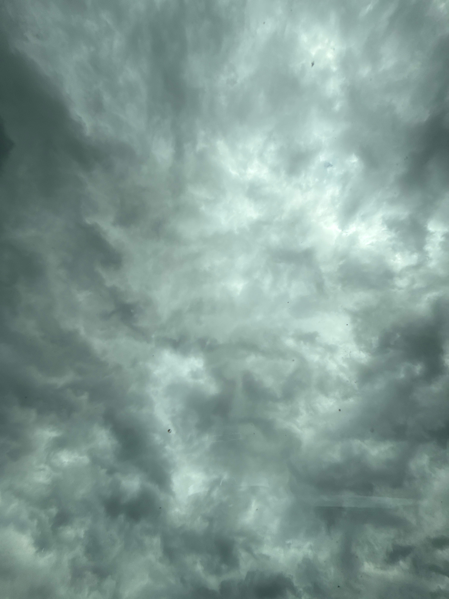 The image depicts a sky filled with dark, heavy clouds, suggesting an overcast or impending stormy weather condition. The clouds are varied in density, with some areas appearing brighter where sunlight is attempting to penetrate, and other areas deeply shadowed and ominous. There are small, dark specks scattered throughout the image, which could be debris, insects, or atmospheric particles. The perspective suggests the photo was taken looking upwards. The image does not contain any identifiable landmarks or features that would place it specifically within the city of Werther, Germany. There are no people, subjects, objects, or actions visible in the scene.