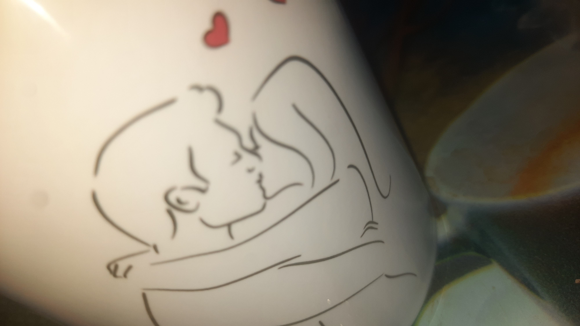 The image shows a white ceramic mug with a line drawing of two people embracing and a heart symbol. The style of the drawing is minimalist and romantic. The mug is illuminated by a light source from the top right, creating highlights and shadows. The background is dark and out of focus, suggesting the mug is placed on a surface. There is no discernible location in the city of Шклоў, Belarus, visible in the image.