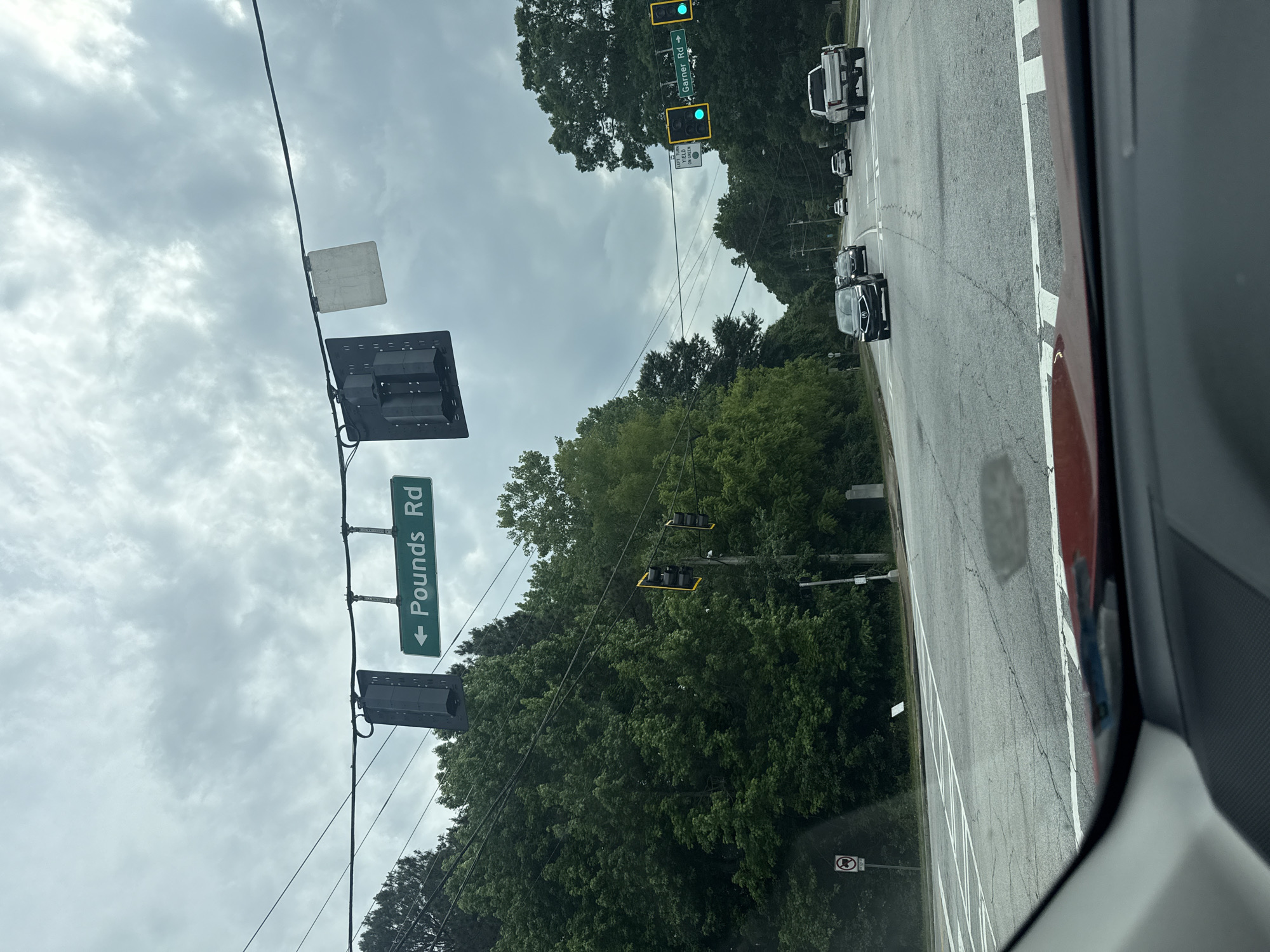 The image shows a street view, likely taken from inside a vehicle. A green street sign indicates "Pounds Rd" with a left arrow. Traffic lights are visible, with one set showing green. Several vehicles are on the road, including a white truck and a dark-colored car. The sky is overcast. The location is identifiable by the street sign as the city of Mountain Park, United States of America.
