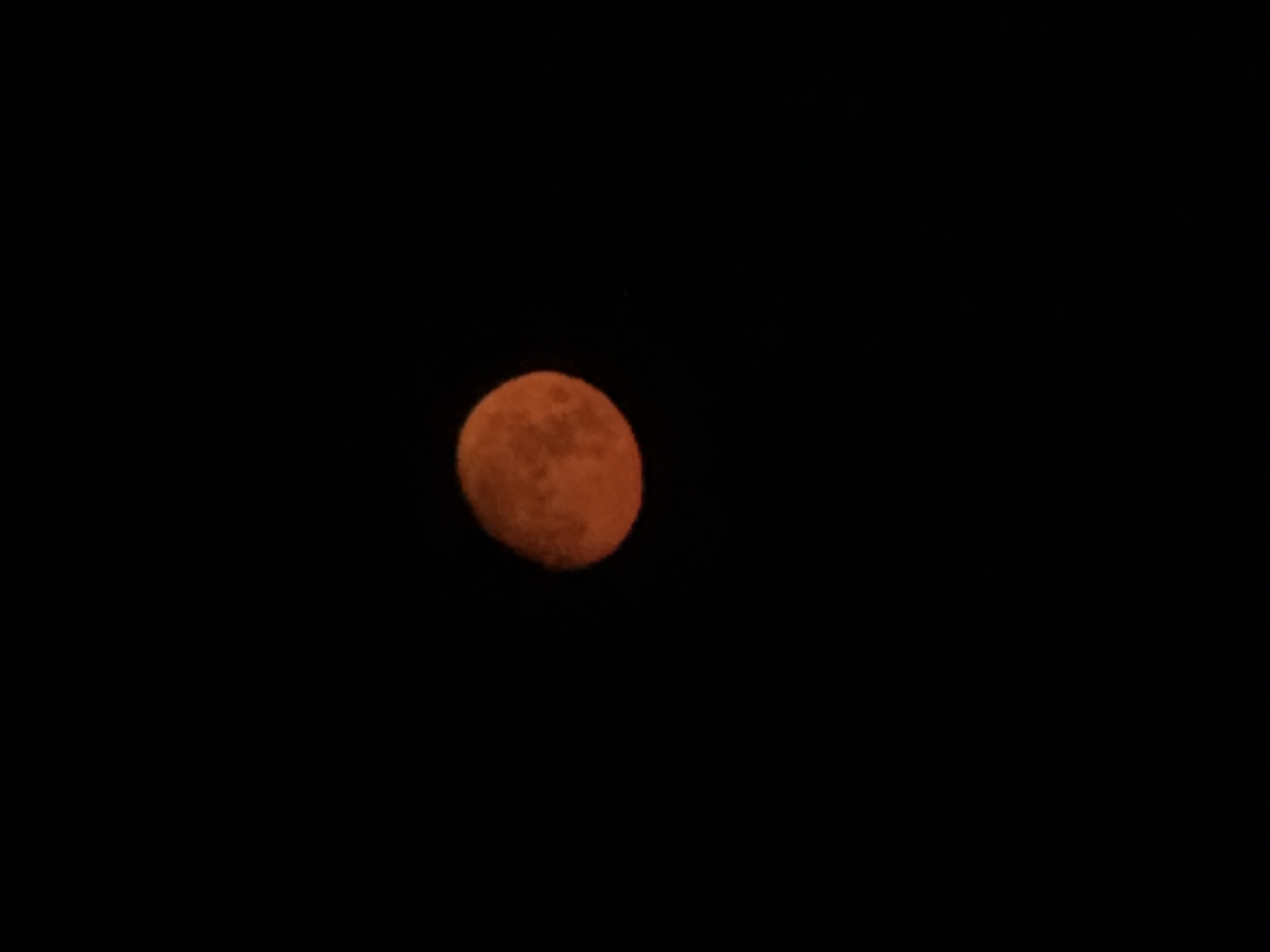 An isolated, orange-colored full moon is seen against a black, night sky. The moon is slightly off-center, situated to the left side of the frame.