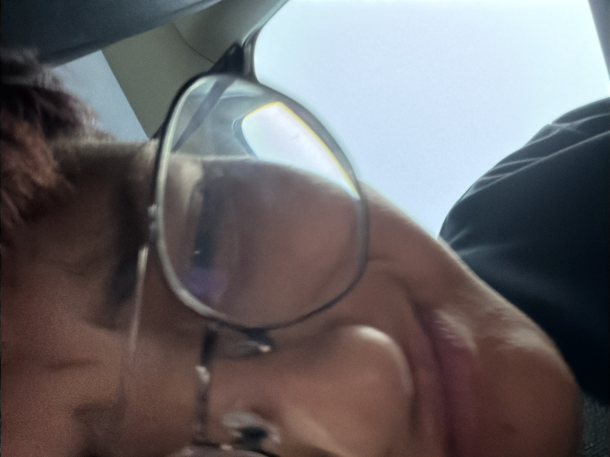 A close-up, slightly out-of-focus, selfie-style photograph shows a person wearing glasses. The subject is looking downwards, and their face is partially obscured by the glasses. The background consists of a bright, hazy sky and a dark-colored garment, possibly a shirt or jacket. The lighting suggests it is daytime, possibly outdoors or in a vehicle with a clear sky visible. The image does not contain any discernible information that would allow for the identification of a specific location in Strömstad, Sweden.