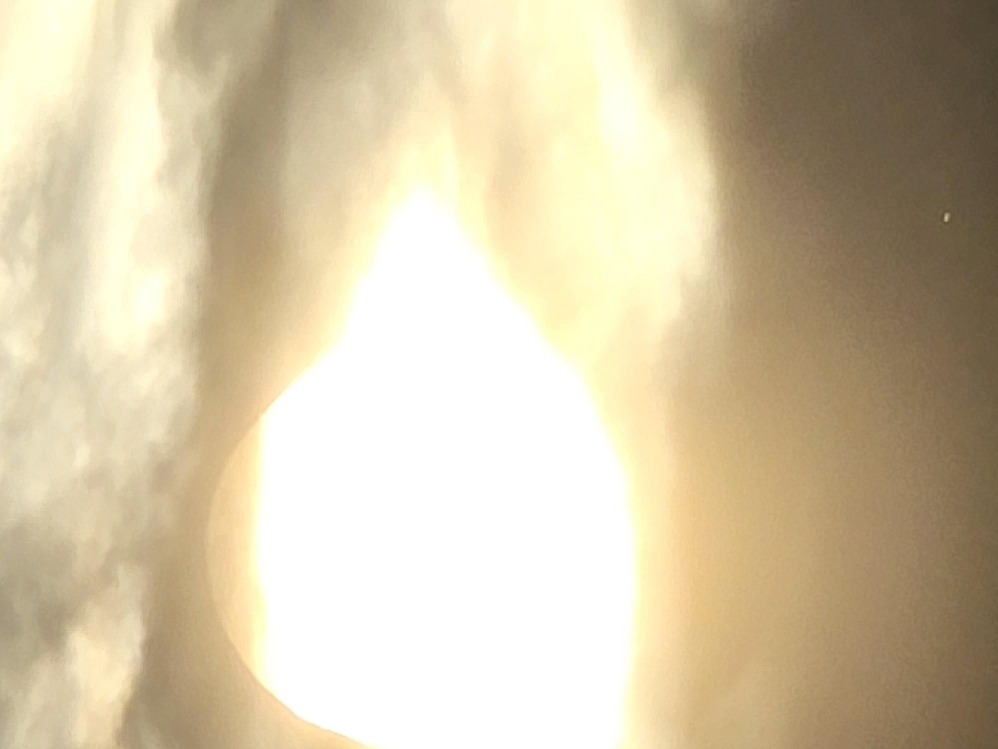 The image depicts a brightly lit area, potentially a sun obscured by clouds. A small object, possibly a distant light or planet, is visible in the darker portion of the image. The location is unknown.