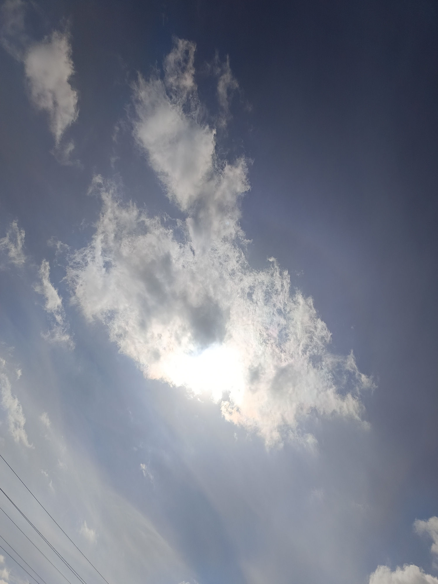 The image shows a sky with scattered clouds. The clouds are mostly white and grey, with some areas appearing brighter due to sunlight. The sky is blue in areas where it is visible between the clouds. In the lower left corner of the image, there are power lines. The location is indicated as the city of Chaikovsky, Russia, but there is nothing in the image itself to confirm this. There are no people or interactions visible in the scene. The environment is a daytime sky with cloud cover.