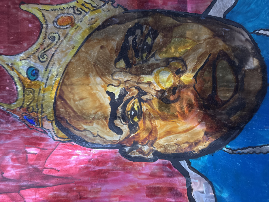This is a photograph of a vibrant, stylized portrait painting depicting the head and upper chest of a man, widely recognized as Christopher Wallace, known as The Notorious B.I.G. The subject faces forward with a somber, direct gaze, his eyes slightly narrowed. He wears a prominent, ornate golden crown adorned with blue, green, and orange jewels, featuring intricate scrollwork. His skin is rendered in varied tones of brown, gold, and amber, with thick black outlines defining his facial features. A blue garment and a silver-colored chain are visible at the bottom of the frame. The background is a textured, glossy red with visible darker drips and streaks, suggesting a painted glass or layered medium. The artwork is located in Paris, France.