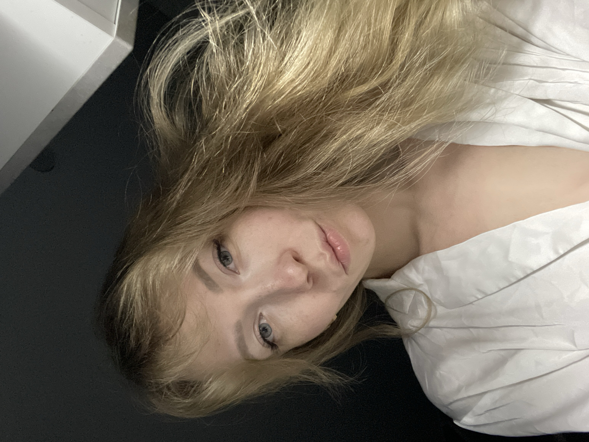 A woman with blonde hair is lying down. She is wearing a white shirt. The background is dark. The location of the city of Perm, Russia cannot be confirmed.