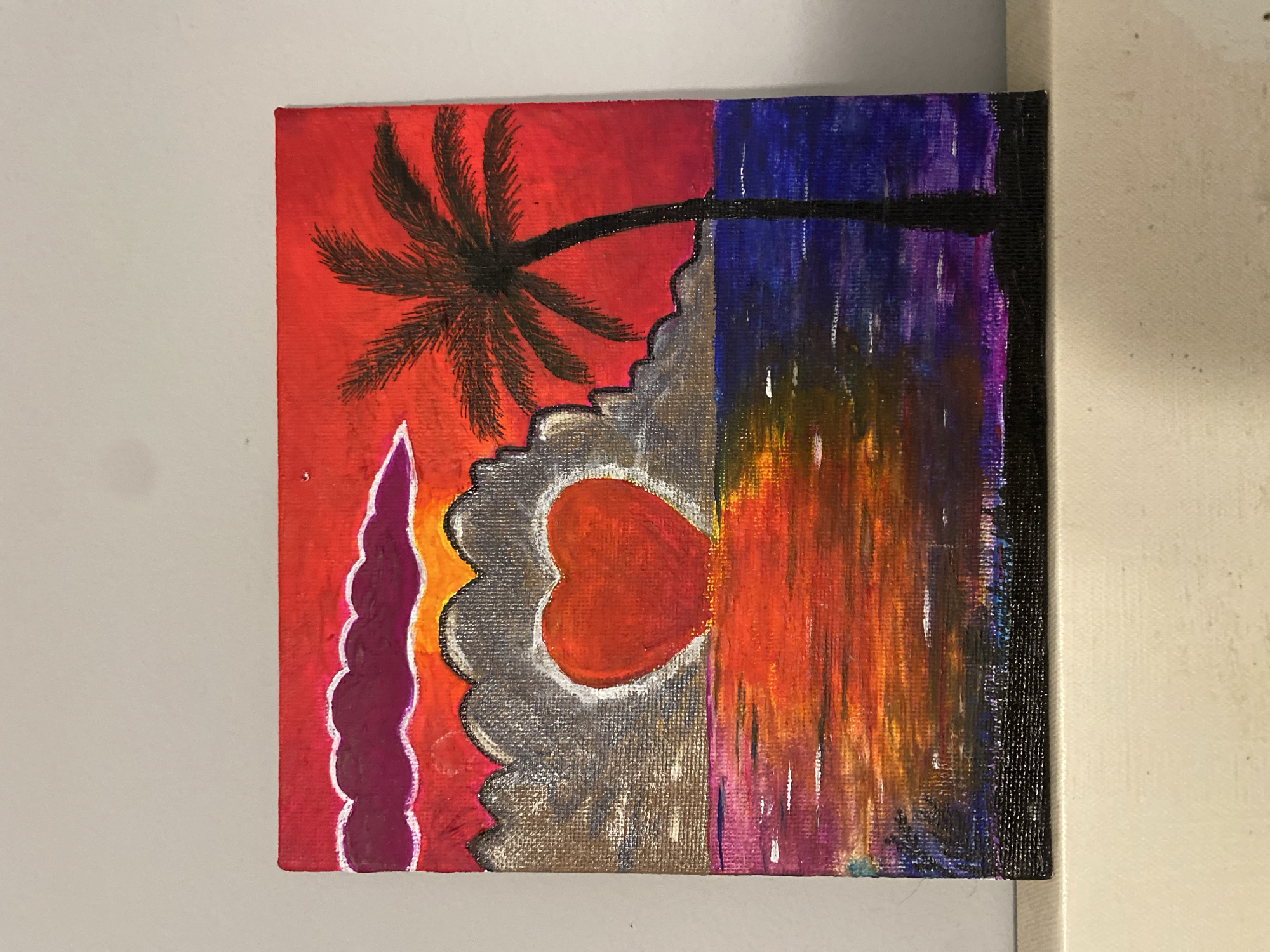 An abstract painting on canvas depicts a sunset scene. The left side features a red and orange sky with a black palm tree silhouette. A grey, cloud-like shape contains a red heart with a white outline. To the left of the cloud is a maroon, scalloped form. The right side of the painting transitions to blues and purples at the top, blending into oranges and reds below, with vertical streaks suggesting rain or reflections. The right edge of the canvas is painted black. The painting is photographed on a gray surface with a white canvas visible in the background. The scene is not set in the city of Sochi, Russia.