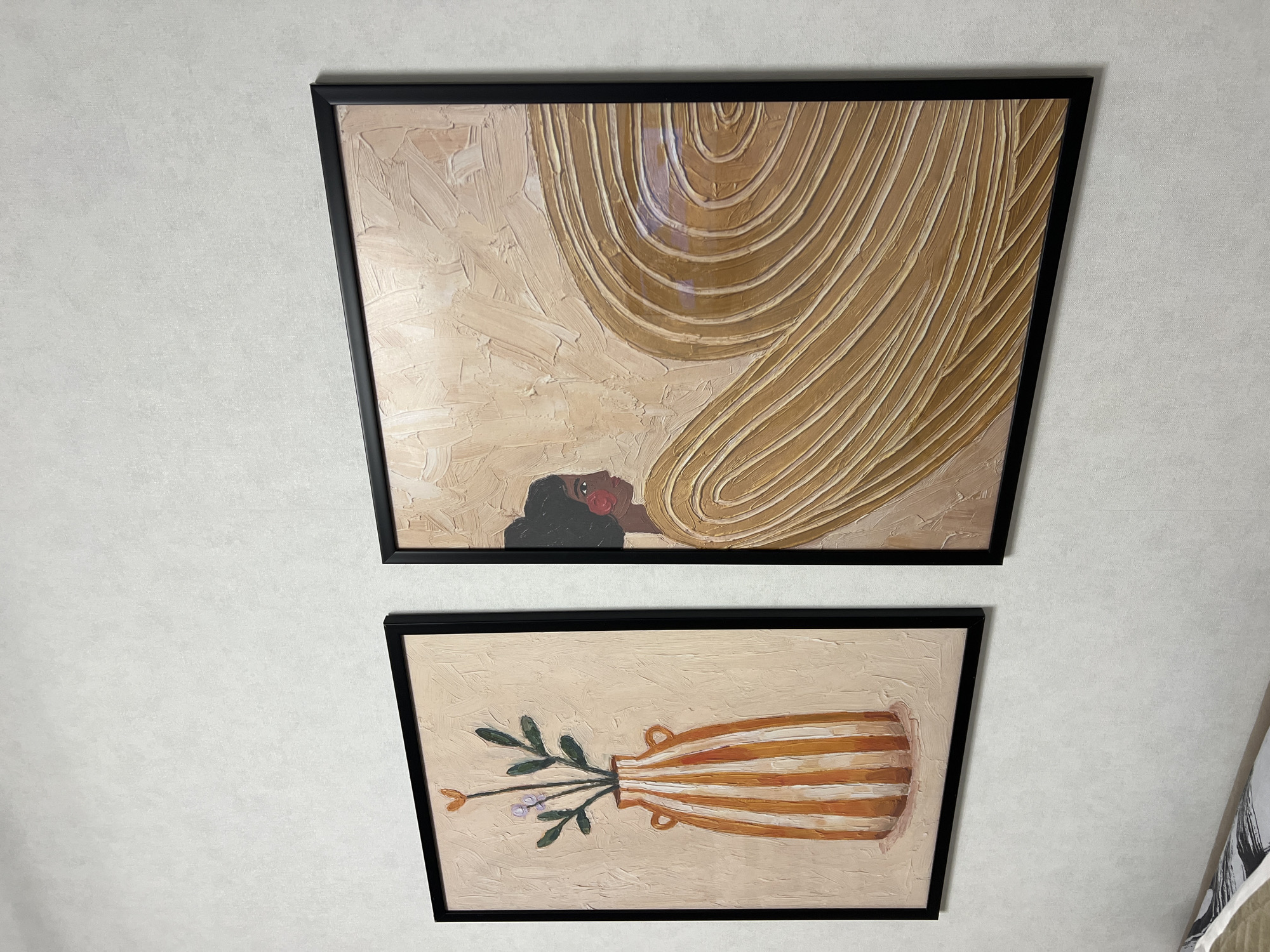Two framed paintings hang on a white wall. The top painting depicts a person lying down with a tan or beige draped fabric. The bottom painting shows a vase with leaves and flowers. The image was taken indoors, likely in a residential setting. There is no verifiable evidence of the location being in Perm, Russia.