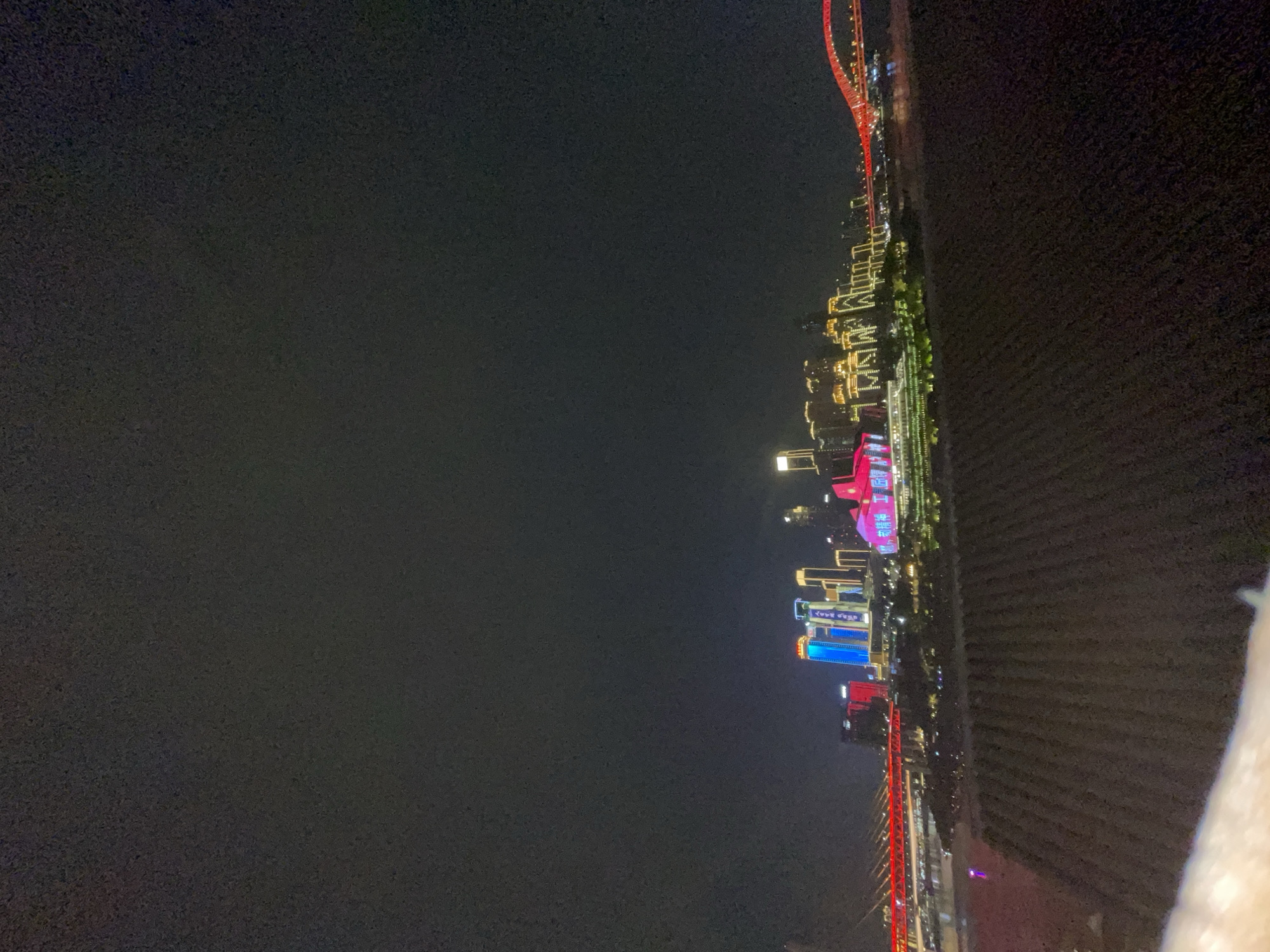 The image shows a nighttime view of Yuzhong District, Chongqing, China. A red bridge structure is visible along the right edge, with illuminated buildings and structures extending into the center of the frame. The left side of the image is predominantly dark, likely showing the night sky. Some buildings have neon lights.