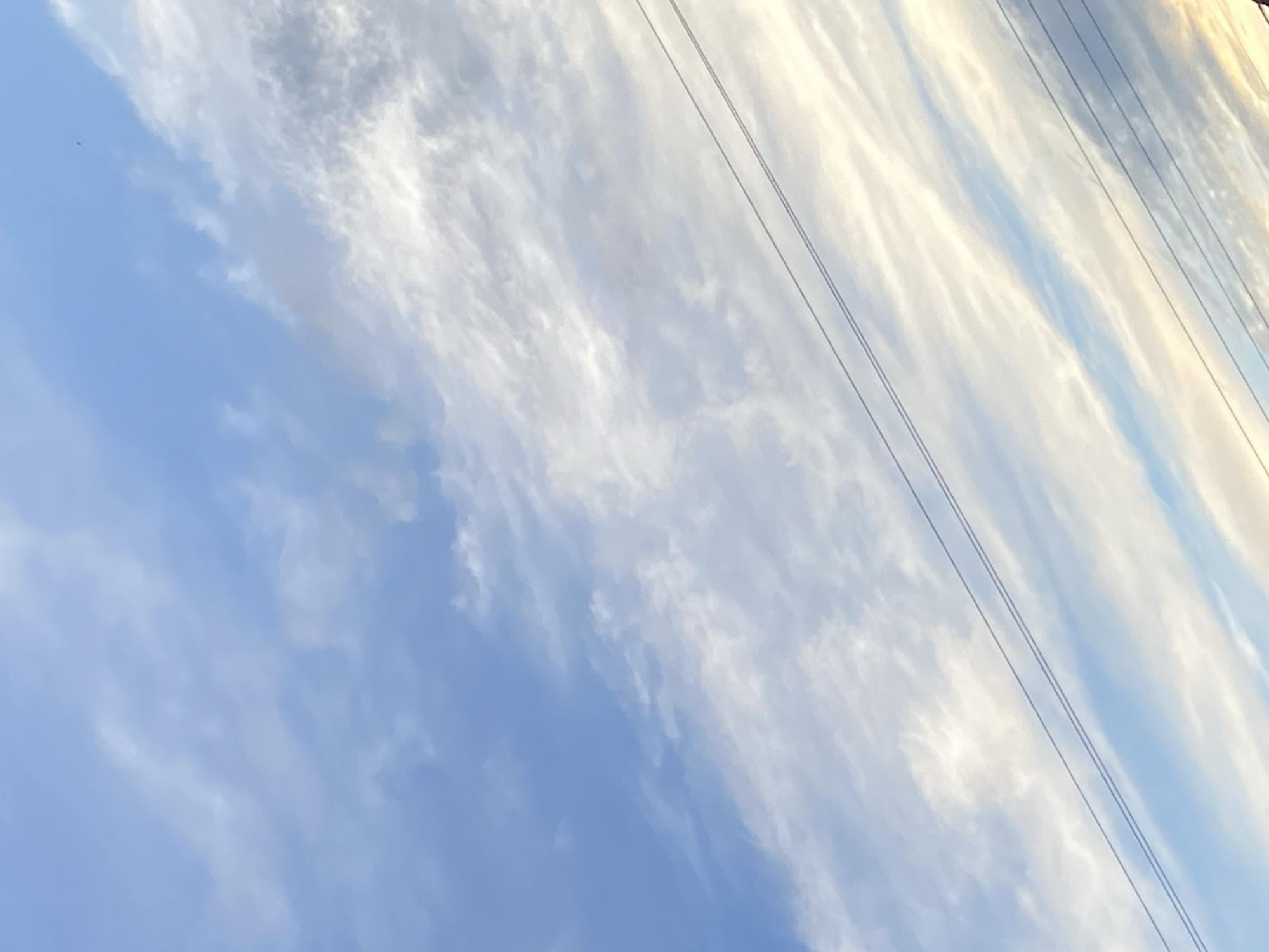 The image shows a daytime sky with blue and white cirrus clouds. Several power lines stretch across the upper right portion of the frame. The location is Tinaquillo, Venezuela.