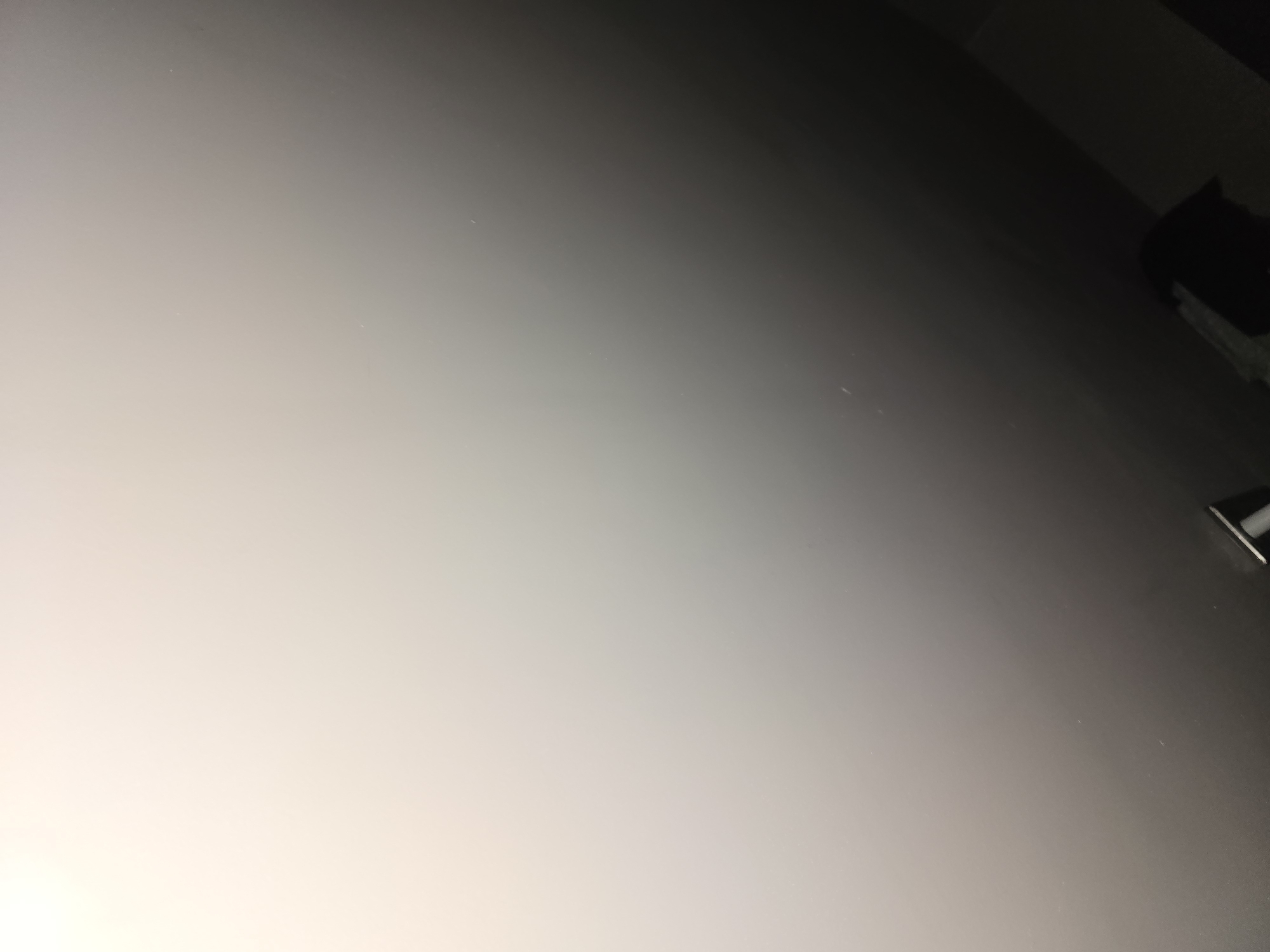 The image shows a dimly lit interior, possibly a room, with a gradient of light from the upper left to the lower right. The surface appears to be a wall or ceiling, with a faint scattering of dust or small imperfections visible. In the lower right corner, a dark, indistinct object or shadow is present, partially obscuring the darker area of the room. No specific location in Ulan-Ude, Russia can be identified from this image.
