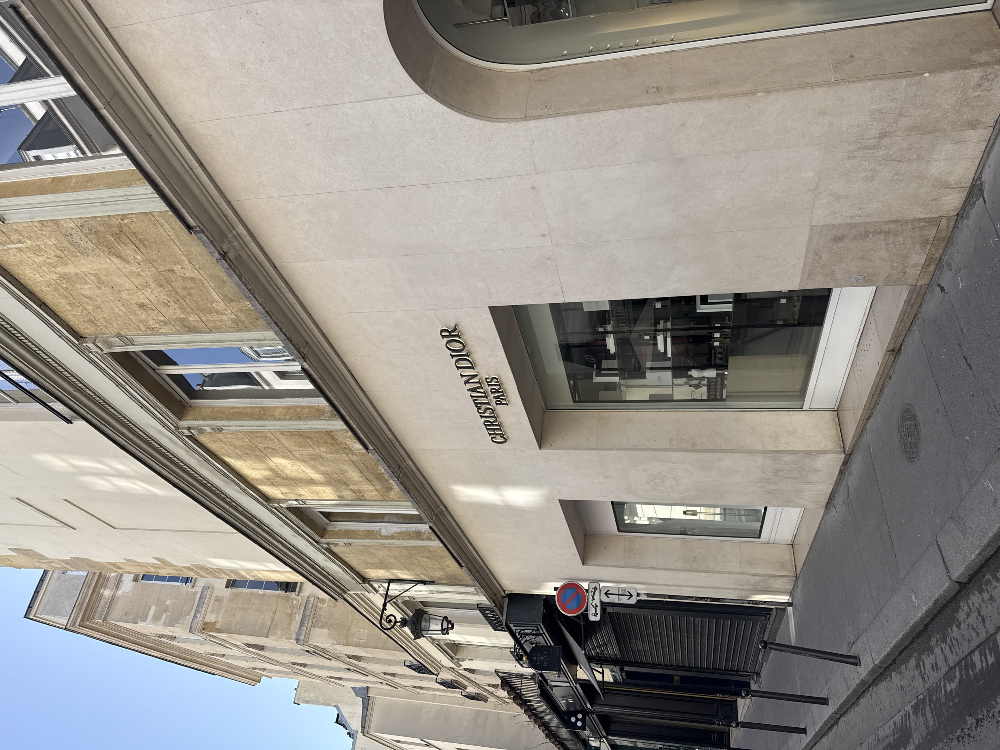 A street level view in Paris, France of the Christian Dior store front sign along with a shop window and the street/sidewalk.