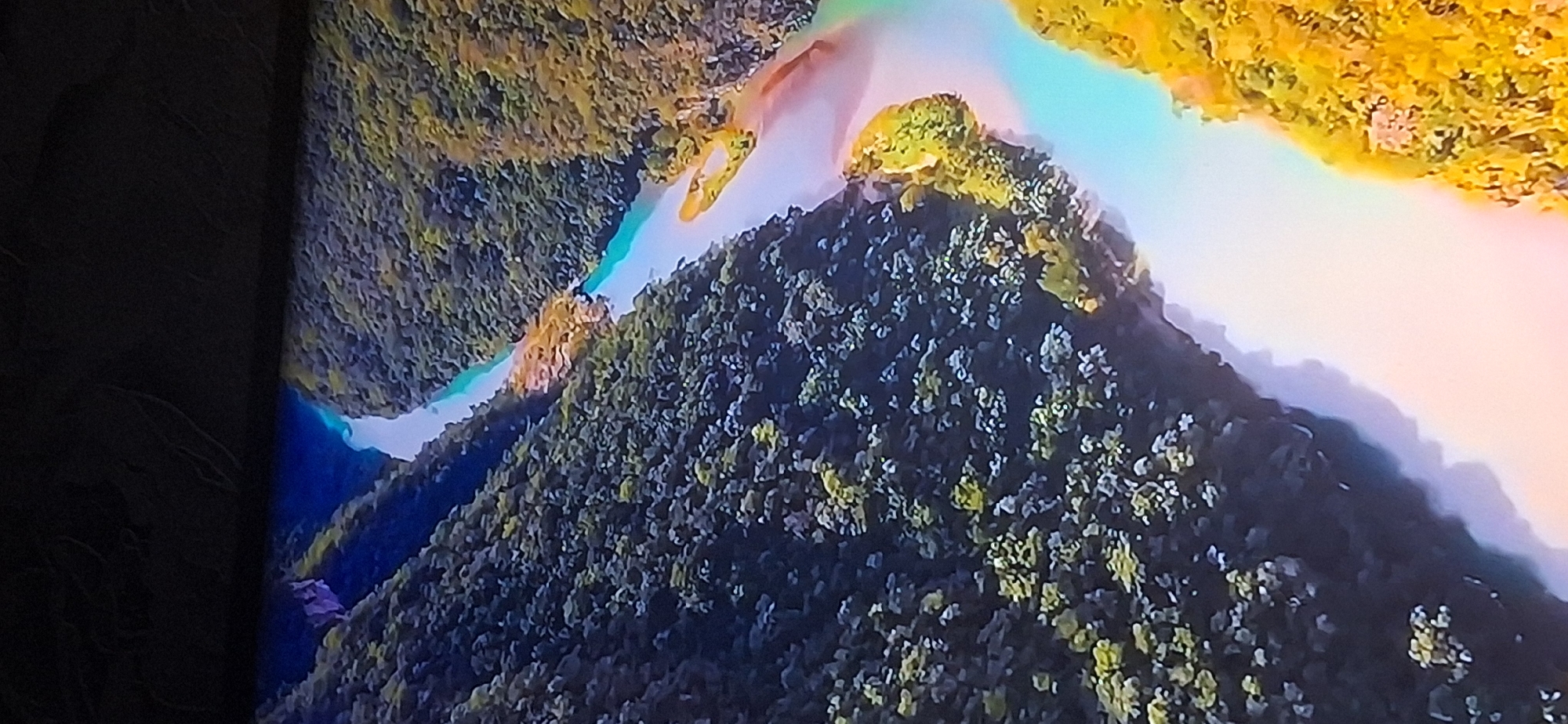 The image shows an aerial view of a vibrant, winding river flowing through a lush, densely forested canyon. The water exhibits a striking turquoise hue, transitioning to lighter shades near the banks. The surrounding landscape is dominated by a rich tapestry of green trees, with patches of golden-yellow vegetation interspersed, particularly on the right side of the river. The terrain appears rugged, with steep inclines covered in foliage. The lighting suggests it's daytime, with shadows cast by the trees adding depth and texture to the scene. There are no visible man-made structures or people in this image.
The provided image is an aerial view of a natural landscape, and there is no information within the image itself to associate it with Bila Tserkva, Ukraine, or any specific city. The scene depicts a river and forested terrain.