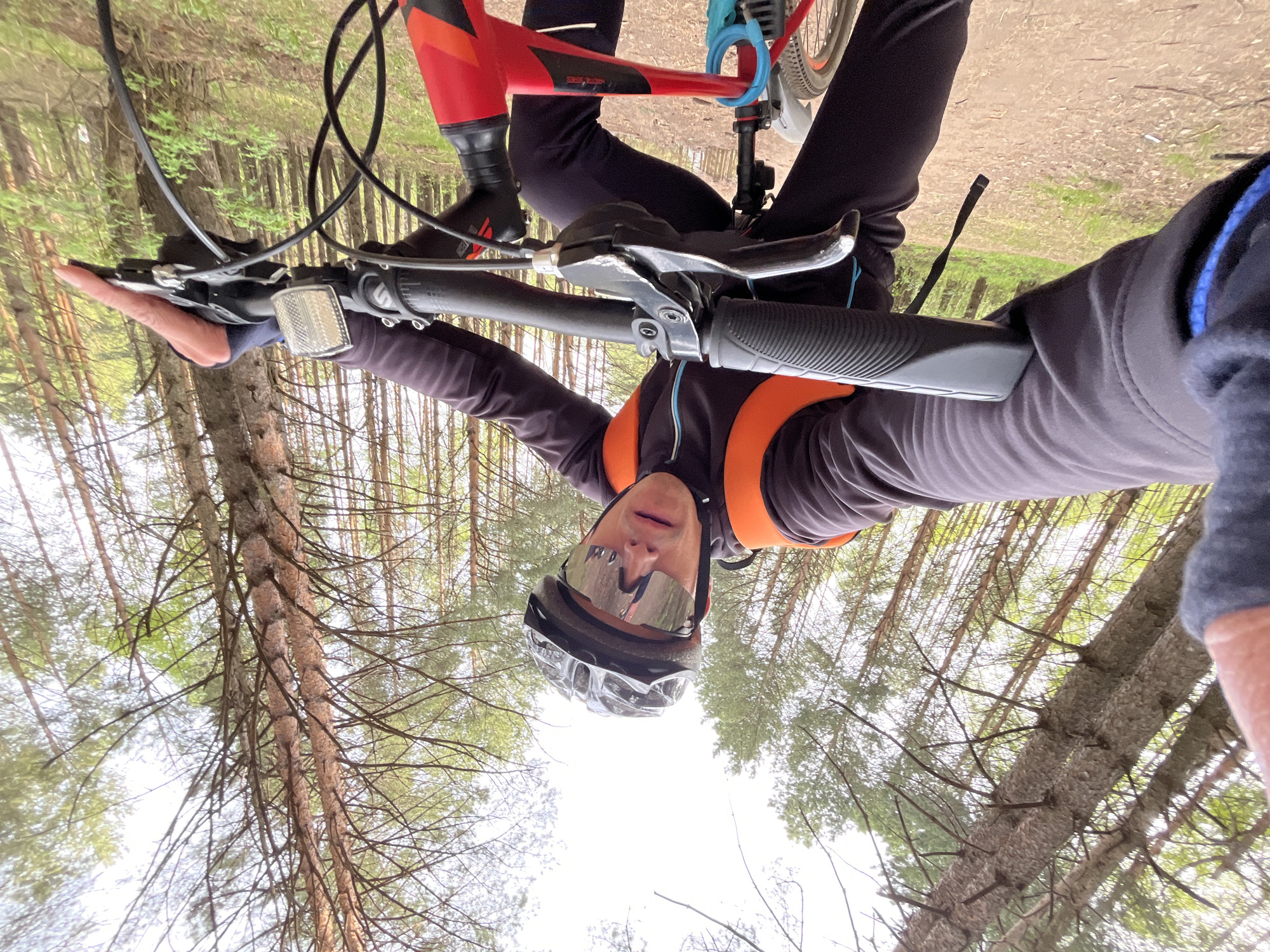 A selfie taken by a person on a bicycle in a forest. The person wears a helmet and sunglasses. The bicycle is red and black. Trees surround the person. The location is Chaikovsky, Russia. The image is oriented upside down.