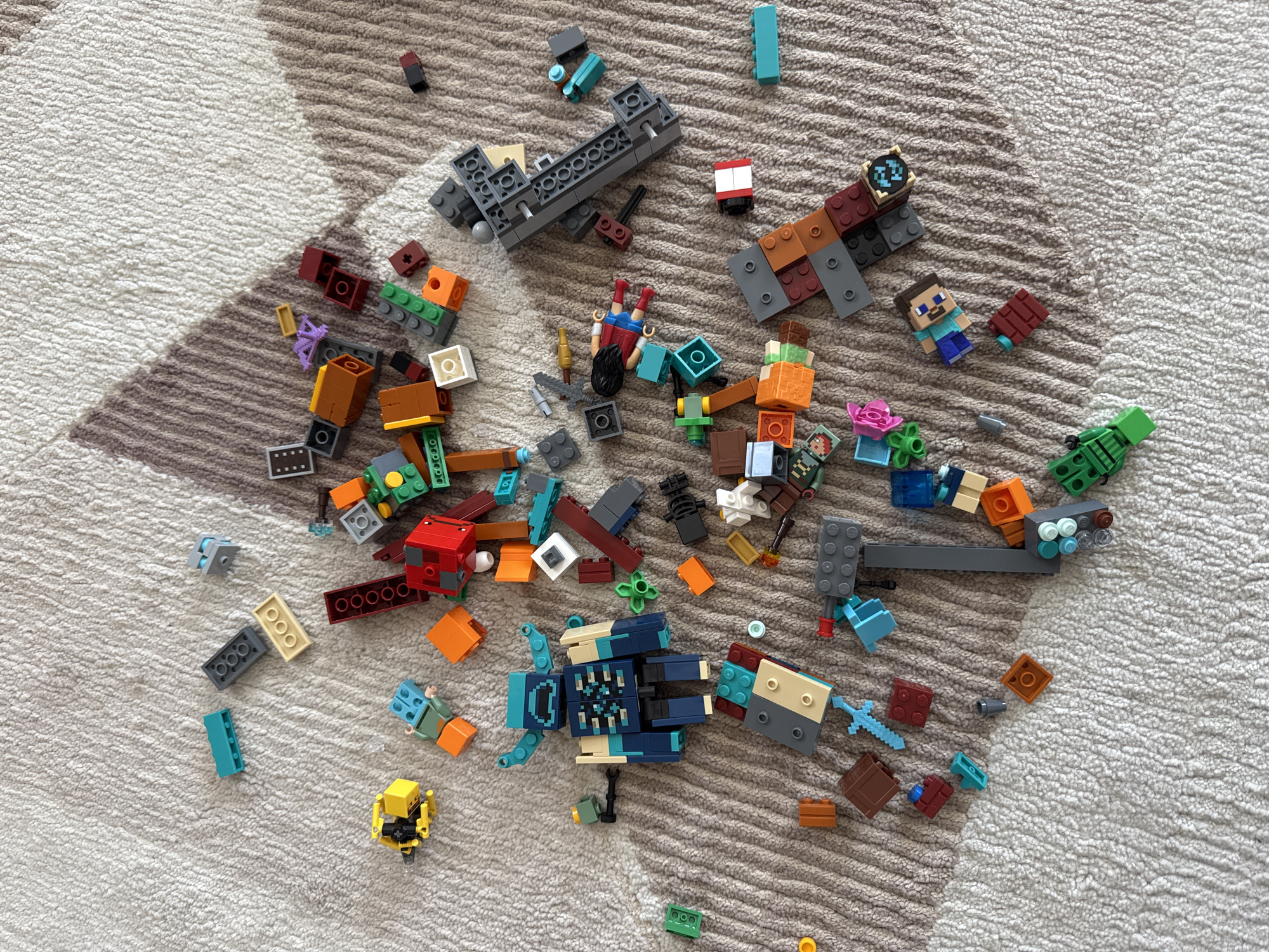 A collection of Lego Minecraft bricks and minifigures are scattered on a neutral-toned patterned rug. The objects include various brick shapes, colors, and sizes, as well as several recognizable Minecraft character minifigures, such as Steve, Alex, and various mobs. The minifigures and bricks are not arranged in any particular order, suggesting a state of disarray or scattered play. The setting is an indoor space on a patterned rug. It is not possible to determine the location within Podgorica, Montenegro from the provided image.