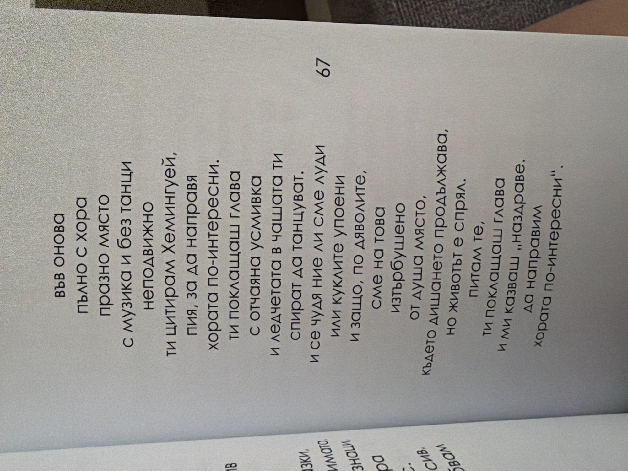 The image shows a page from a book with Bulgarian text. The text is printed in a dark font on a light-colored, textured paper. There is a page number "67" in the lower right corner. The left side of the image shows a sliver of another page with some vertical text. The overall scene is an indoor environment, likely a room where someone is reading or holding a book. There is no visible information in the image that relates to the city of Pazardzhik, Bulgaria.
