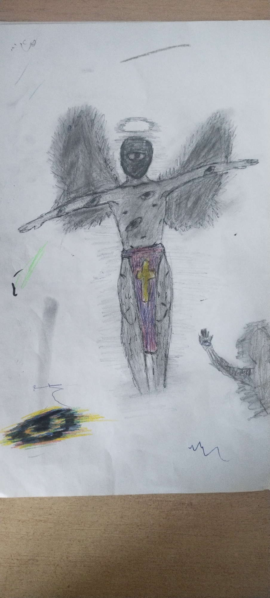 A pencil drawing on white paper depicts an angelic figure with dark, feathery wings outstretched. The figure has a halo above its head and wears a mask that obscures its face, with a single eye visible. A draped cloth with a purple and gold cross adorns its waist. To the left, a faint green light emanates from a curved line. In the lower left corner, there's an abstract, colorful mark. To the right, a shadowy figure with an outstretched arm appears to be reaching towards the angelic figure. The drawing is rendered in shades of gray and black, with hints of color on the cross and the abstract mark. The background is predominantly white, suggesting a cloudy or ethereal environment. The drawing is placed on a surface that appears to be a wooden table. There is no information in the image that would indicate its location in Pisochyn, Ukraine.