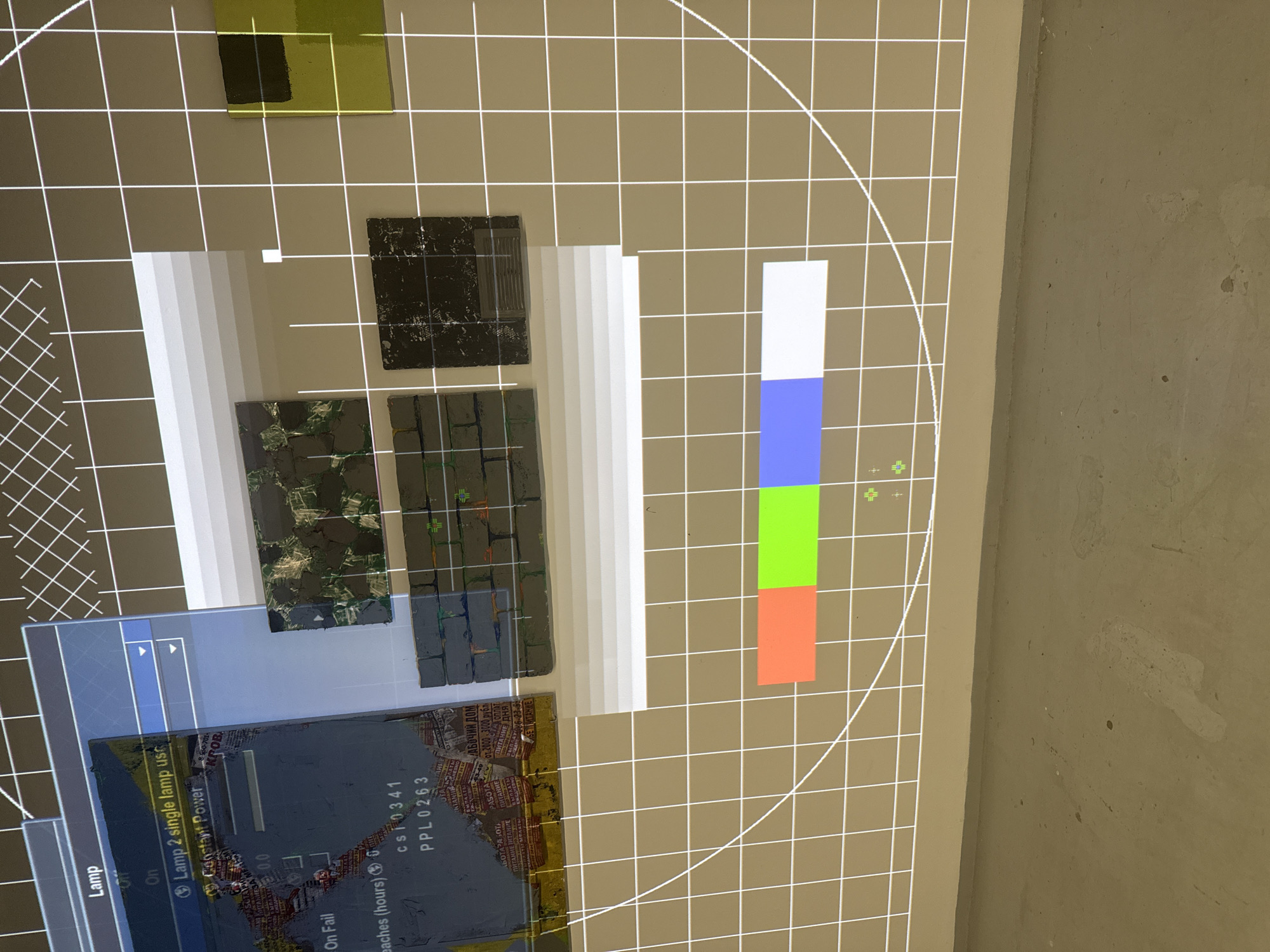 The image shows a variety of objects placed on a gridded surface, possibly for documentation or examination. These objects include colored swatches of white, blue, green, and orange, along with tiles or samples displaying different patterns and textures, ranging from dark and structured to those with an organic, mossy appearance. A digital interface overlay is present, displaying system controls related to lighting, specifically showing settings for "Lamp 2" and a "Constant Power" option, alongside data on usage hours and codes "cs10341" and "PPL0263". Notably, a printed image is partially visible, displaying what appears to be urban landscape and text in Russian Cyrillic script, with the phrase "РАБОЧИЙ ДОМ" ("WORKER'S HOUSE") and references to monetary amounts in rubles, suggesting a location in Moscow, Russia. The environment surrounding the objects is plain, with a visible wall or surface in the background.