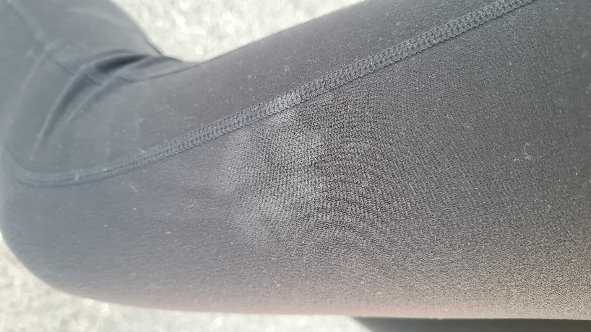 The image shows a close-up of a person's leg wearing black leggings. The leggings have a lighter, faded patch on the thigh area. The fabric is textured and shows stitching at the seam. The background is out of focus but appears to be a light, possibly concrete surface. There is no information to determine the location is Lachish Regional Council, Israel.