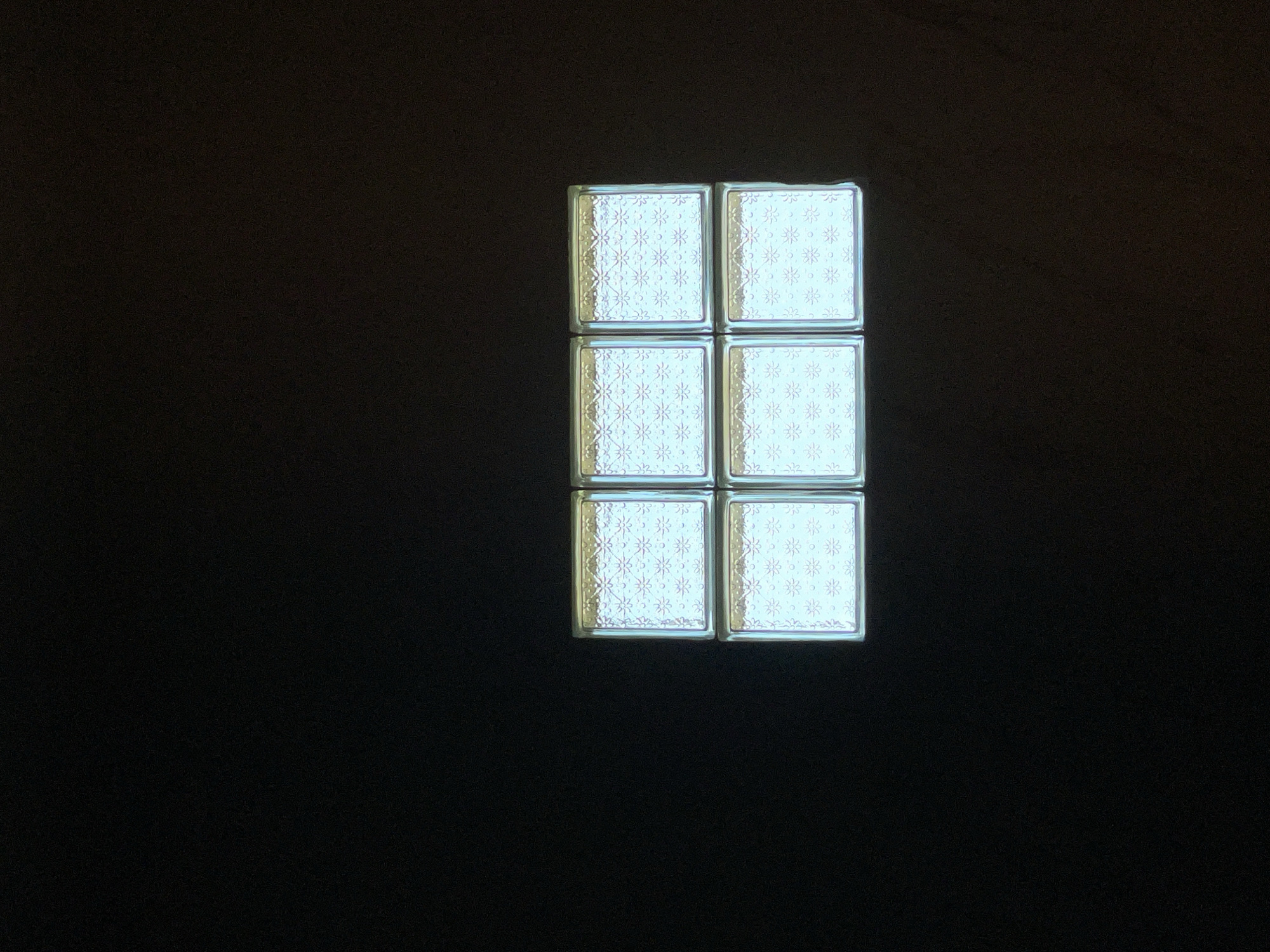 The image shows a close-up of six glass blocks arranged in a two-by-three grid. The blocks are translucent with a patterned texture, and they appear to be illuminated from behind, casting a soft glow. The background is entirely black, suggesting a dark environment or a photograph taken in low light conditions. There is no indication of the city of Kediri, Indonesia, or any other specific location. The scene is static and devoid of any human presence or activity.