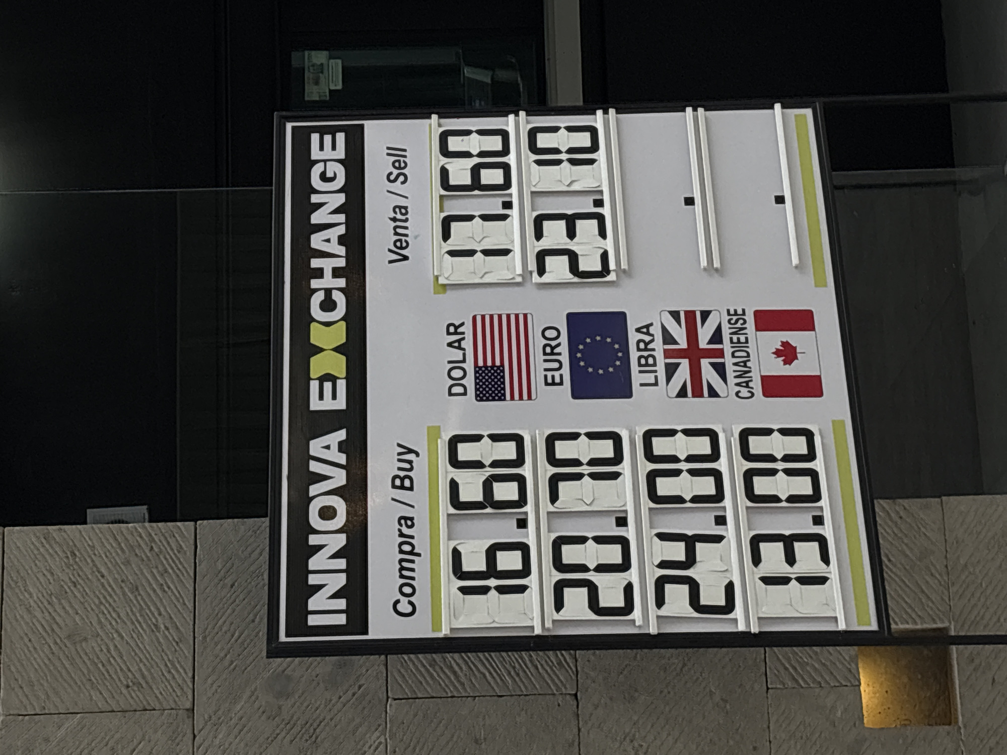 The image shows an exchange rate display for INNOVA EXCHANGE. The display indicates the "Compra/Buy" and "Venta/Sell" rates for various currencies. The rates are displayed using a digital number display. The image shows the U.S. dollar, the Euro, the British Pound and the Canadian dollar. The rates for the "Compra/Buy" side are as follows: $16.60 for the U.S. dollar, $20.70 for the Euro, $24.00 for the British Pound, and $13.00 for the Canadian dollar. The "Venta/Sell" rates displayed are $17.60 for the U.S. dollar, and $23.10 for the Euro. The other selling rates are not available. The image was taken in Ciudad López Mateos, Mexico.