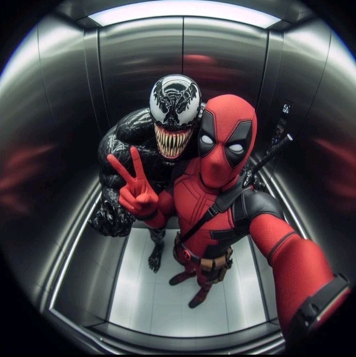 A fisheye lens photo taken from a cellphone shows two people dressed as comic book characters in an elevator. The person on the left is dressed as Venom, a black symbiote character. The person on the right is dressed as Deadpool, a red and black anti-hero. The person dressed as Deadpool is taking a selfie. The elevator has a stainless steel finish. The photo was likely taken in an elevator in a building in the city of Geneng, Indonesia, which is located at latitude -7.45472, longitude 111.427584.