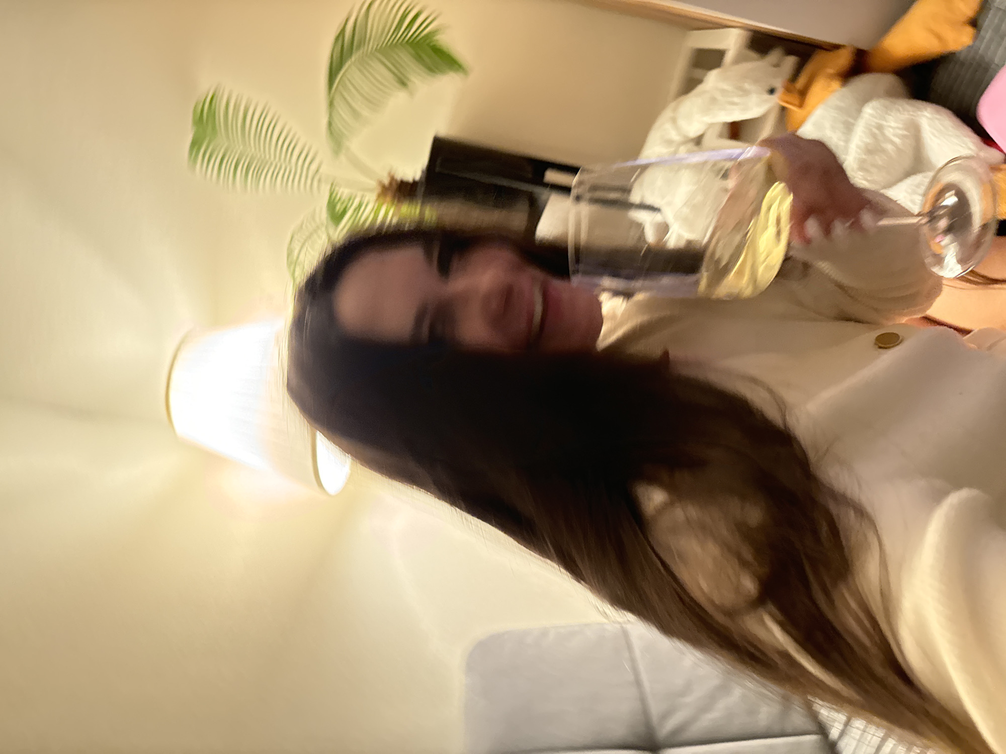 The image shows a woman holding a wine glass, seemingly indoors. Her hair is long and dark. The background features a lamp, a plant, and what appears to be furniture. The location of the image is not discernible from the provided visual content, so it's impossible to pinpoint the location as Odintsovo, Russia.