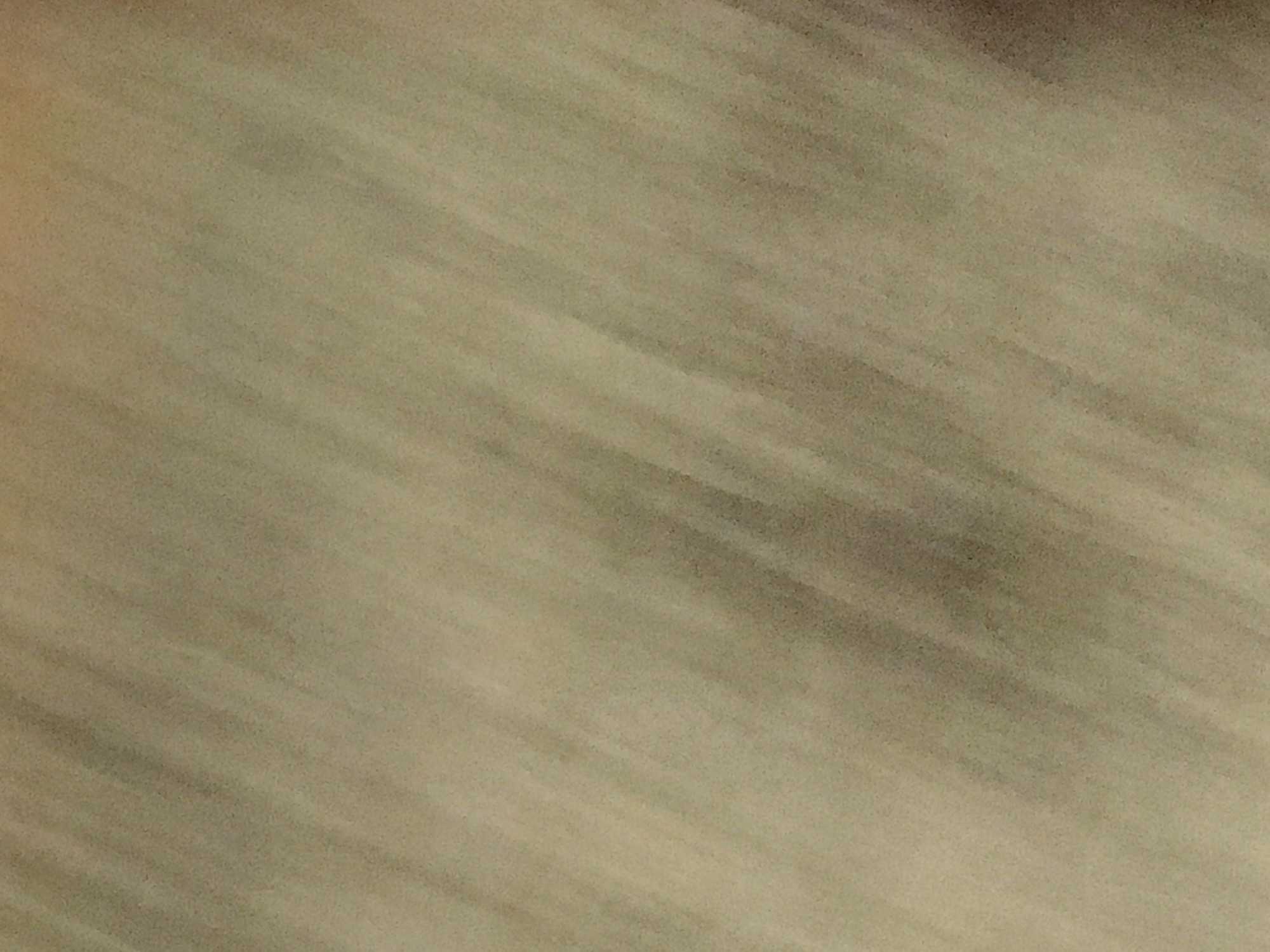 The image displays a close-up, blurred view of a surface with a muted, tan-to-brown color gradient. The texture appears smooth with subtle variations in tone that give it a linear, slightly diagonal pattern. It is not possible to extract information about the location or any objects/people/actions.