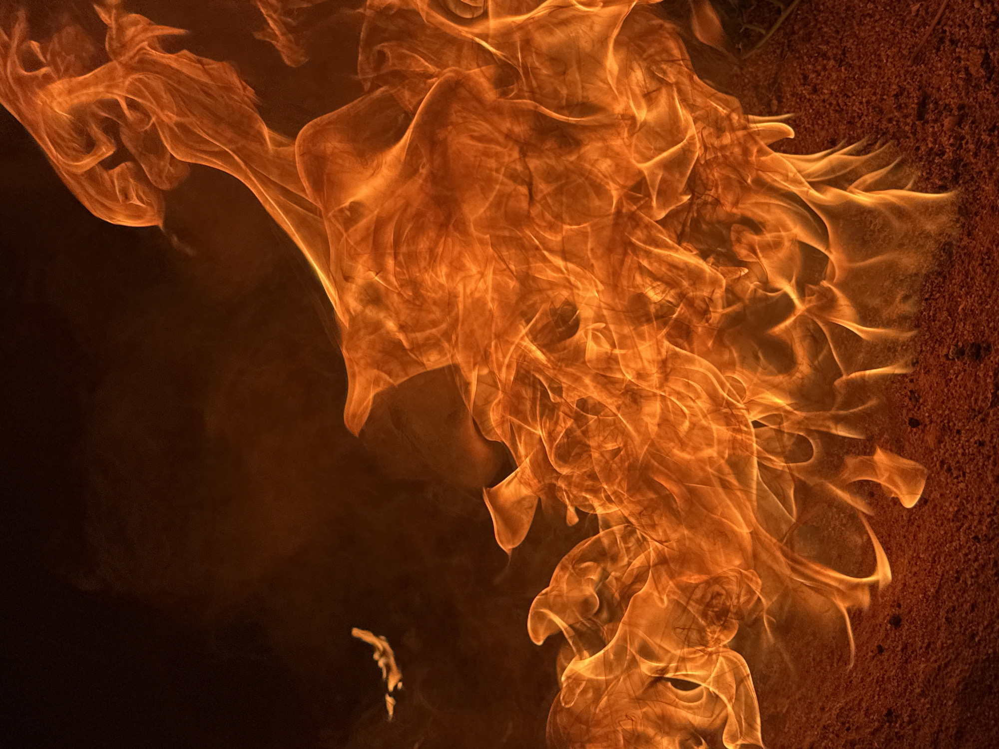 The image shows a close-up view of flames, predominantly orange and yellow in color. The flames appear to be consuming something with dark material on the left side of the image and reddish-brown material on the right side. There is no information available in the image to connect it to the city of Bar Gada, Nigeria, or any people.