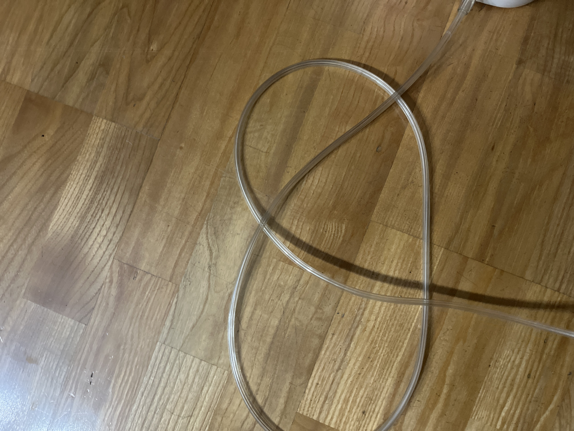 The image shows a clear plastic tube lying on a wooden floor. The tube is looped and crossed over itself, forming a figure-eight shape. The floor appears to be made of hardwood planks with a visible wood grain. There are no people or other objects clearly visible in the frame. The lighting suggests an indoor environment, possibly a room. The location in Saratov, Russia, cannot be determined from the visual information provided.