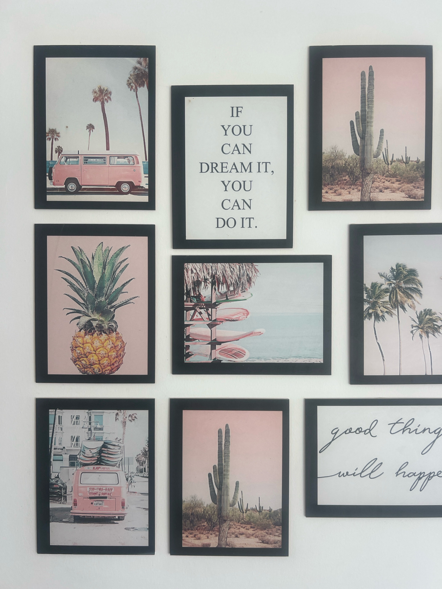 The image displays a grid of nine framed pictures on a white wall. The frames are black and are arranged in three rows of three.
The top row features:
1. A pink van with surfboards on top, parked on a street with palm trees and a beach in the background.
2. A black and white text-based image with the quote "IF YOU CAN DREAM IT, YOU CAN DO IT."
3. A desert landscape with saguaro cacti under a pink sky.
The middle row features:
1. A close-up of a pineapple.
2. A scene with what appears to be lounge chairs and umbrellas at a beach or poolside, with a calm body of water in the background.
3. A tropical scene with palm trees swaying against a light sky.
The bottom row features:
1. A pink van with surfboards on its roof, seen from the rear, driving on a street with buildings and palm trees.
2. Another desert landscape with saguaro cacti, similar to the one in the top row, under a pink sky.
3. A framed image with handwritten text that reads "good things will happen."
There are no people or animals visible in any of the framed pictures. The overall style suggests a collection of decorative art or photographs. The location is not specified within the image itself or the provided context.
