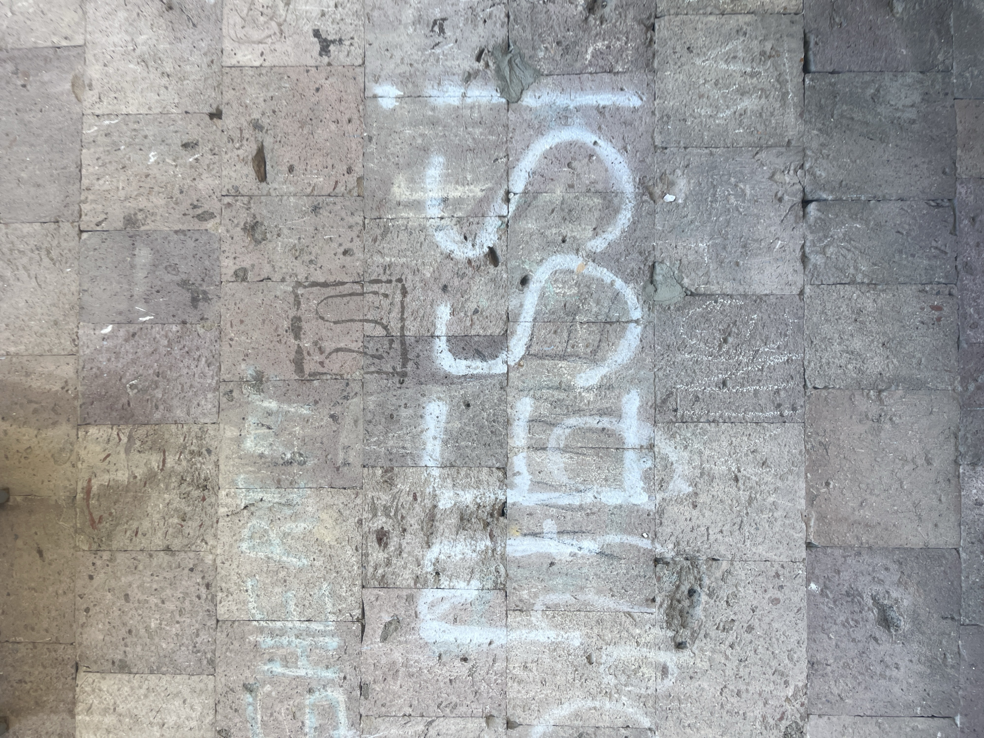The image shows a gray stone tiled ground in Yerevan, Armenia. White graffiti, partially faded, is visible on the tiles. The graffiti includes a numeral "58" with a horizontal line above it.