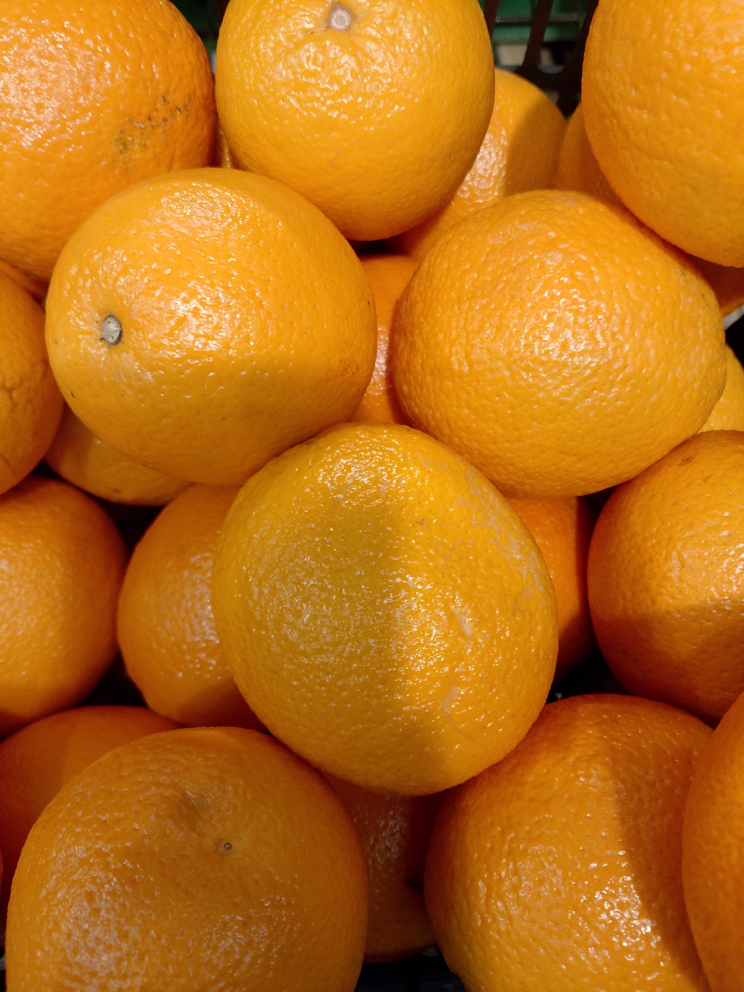 A close-up shows a pile of oranges. The oranges are round and orange in color, and their surfaces have a textured appearance. The lighting appears to be artificial. There is no evidence in the image to suggest it was taken in Chaikovsky, Russia. There are no people, actions, or interactions visible. The objects are simply oranges in a pile.