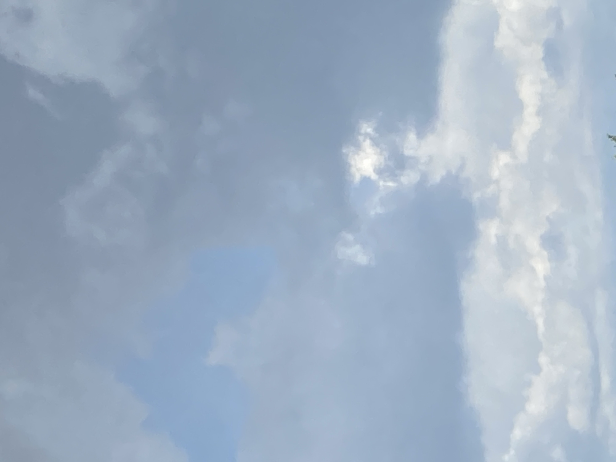 An overcast sky with scattered clouds. A bright patch of sunlight pierces through a break in the clouds, illuminating a portion of the sky. The overall impression is one of a dynamic and ever-changing atmosphere.