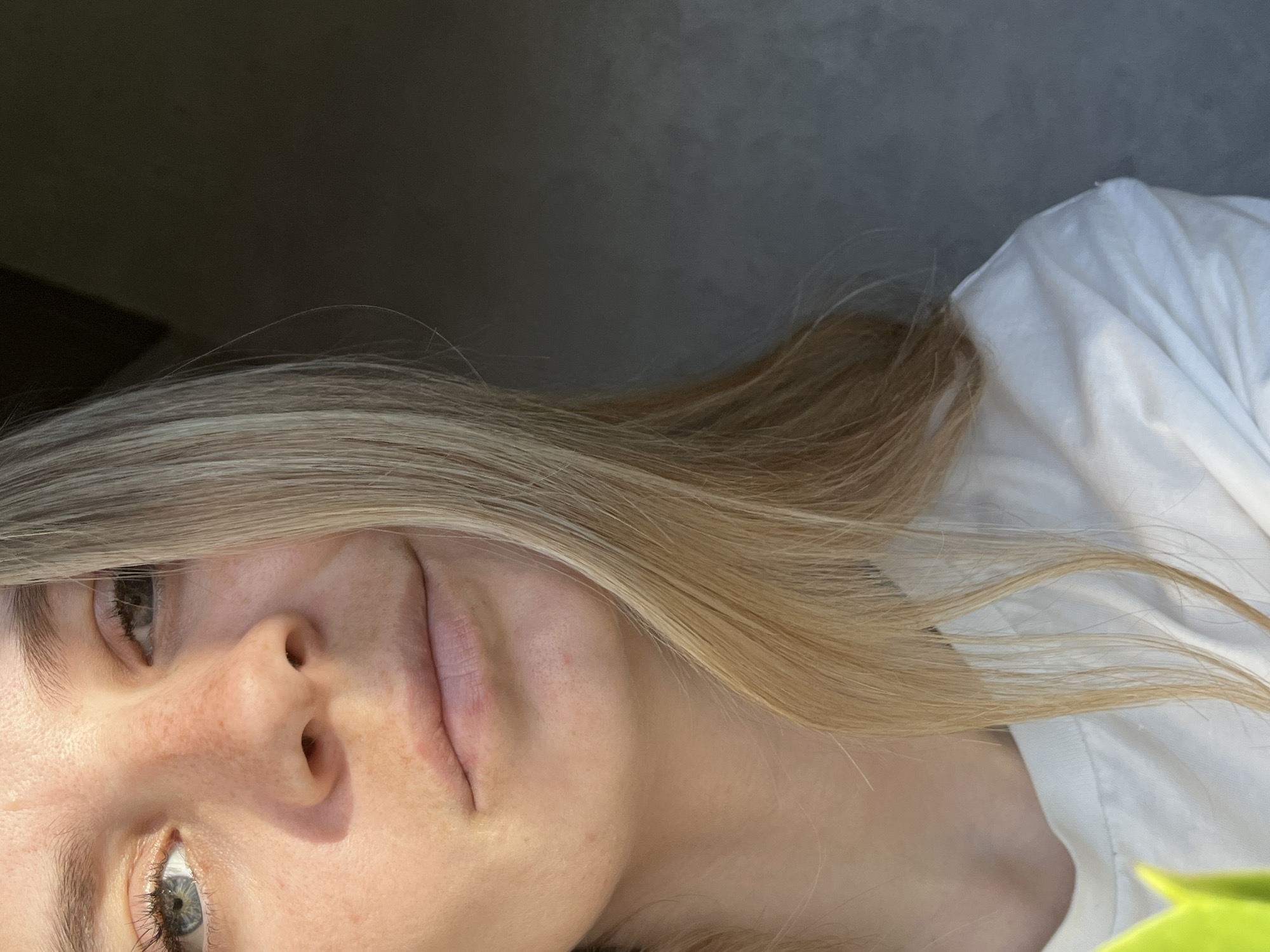 A close-up, tilted shot shows a fair-skinned person with blonde hair. The person's face is prominent, featuring a nose with freckles, lips, and eyes with a hint of green. The person is wearing a white t-shirt. The background is a plain, grayish color. There's no discernible information to indicate the location is Chaikovsky, Russia.