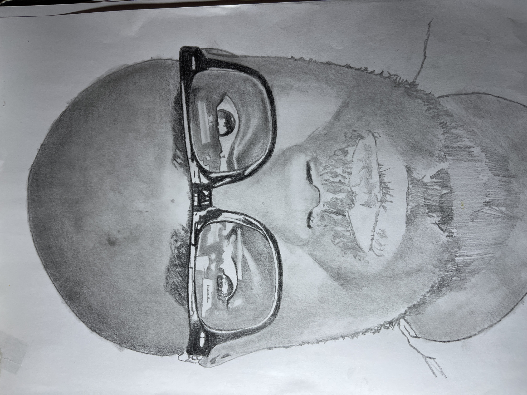 A pencil drawing depicts a portrait of a man with a shaved head wearing glasses. The drawing is detailed and shaded, showcasing reflections in the lenses of the glasses. No features indicate a location in Jos, Nigeria.
