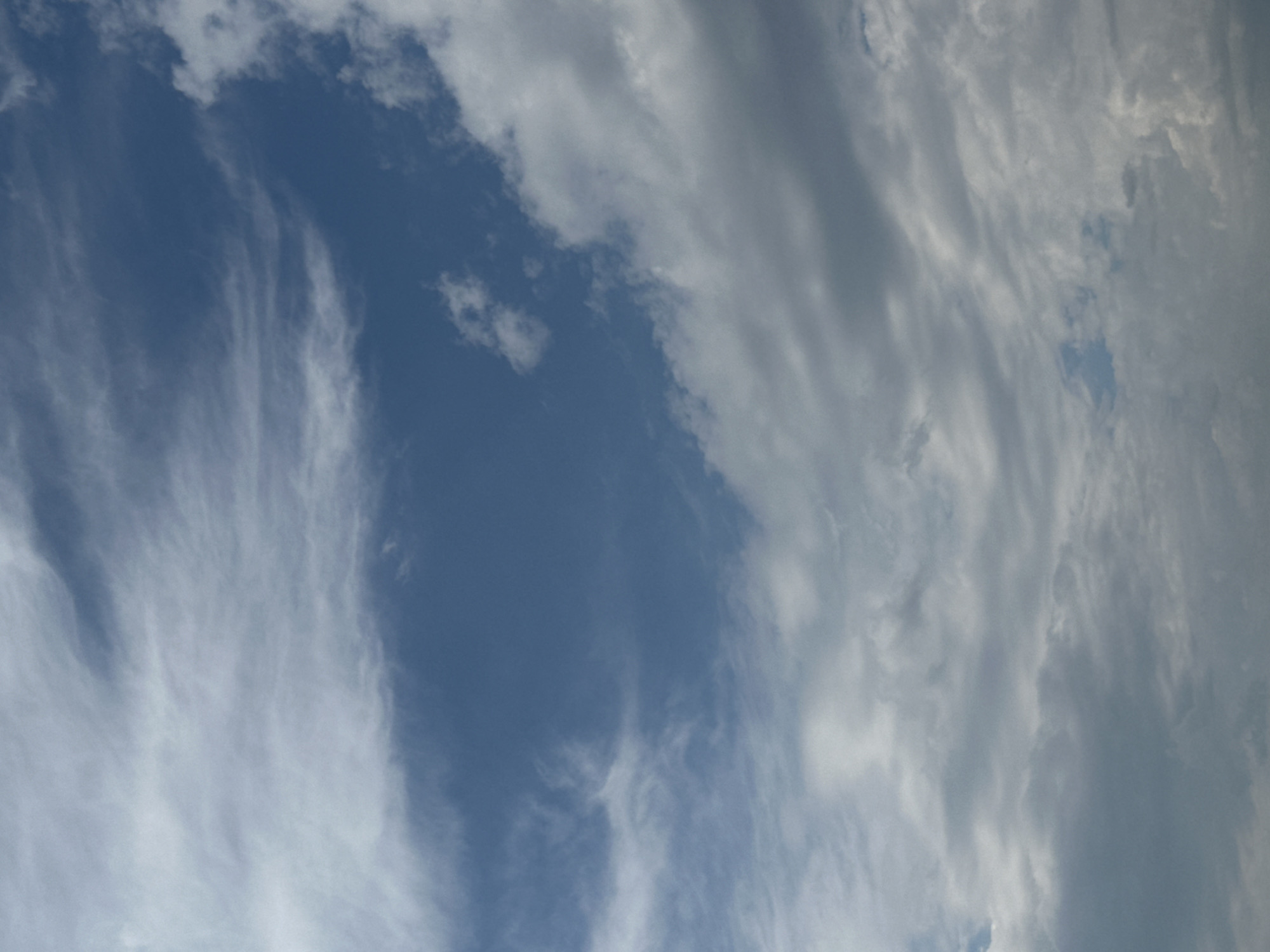 The image shows a sky filled with clouds. The sky is a deep blue, with various shades of white and gray clouds scattered throughout. Some clouds are wispy and thin, while others are thick and dense. The clouds are arranged in layers, with some appearing closer to the viewer and others further away. The overall impression is one of a dynamic and changing sky. There are no people, objects, or man-made structures visible in the image. The image is a natural landscape shot of the sky.