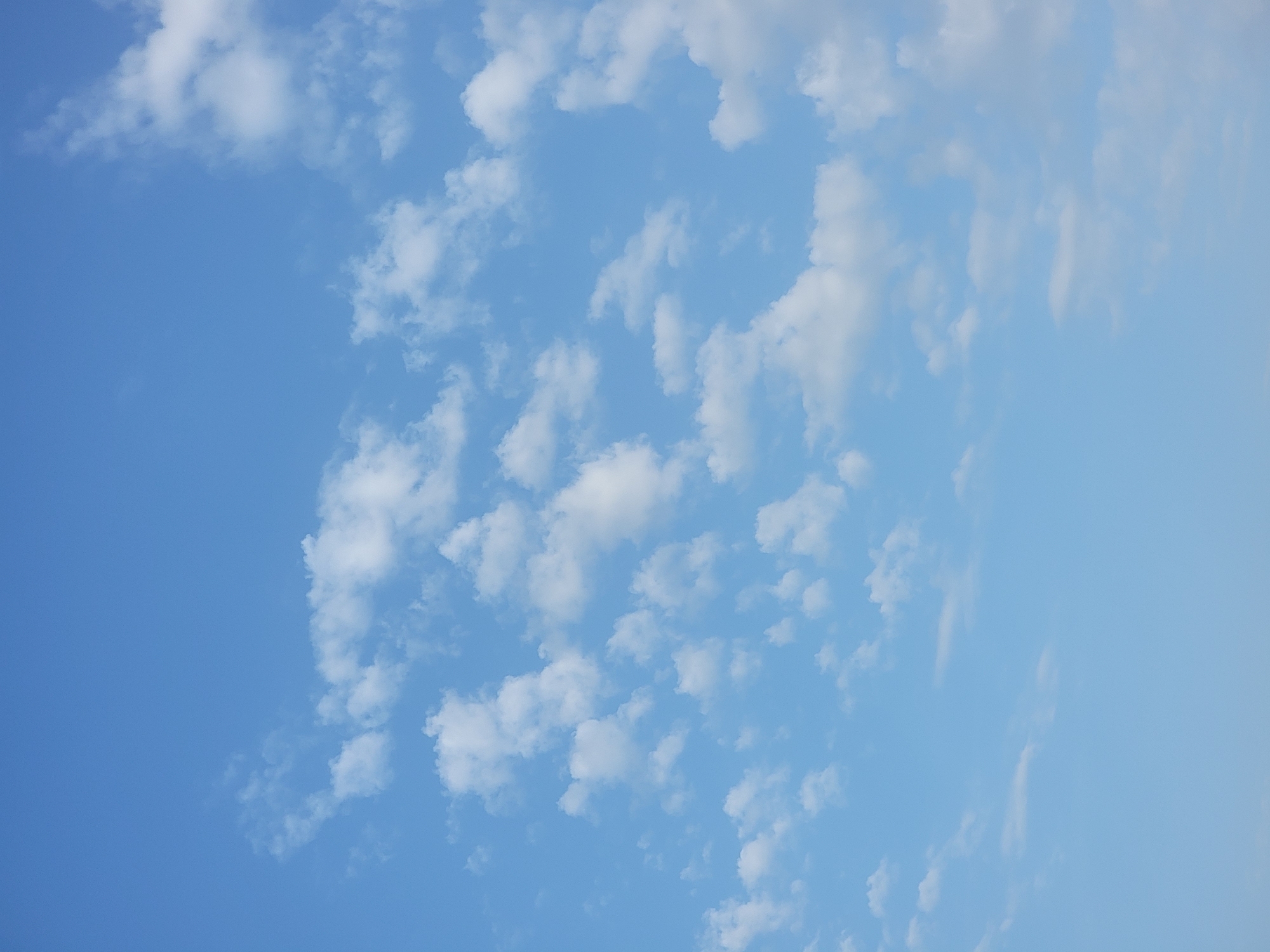 The image shows a clear blue sky with scattered white cumulus clouds. There are no people, subjects, objects, or actions depicted. The environment is an outdoor sky scene. No specific location in Quarteira, Portugal can be determined from this image.