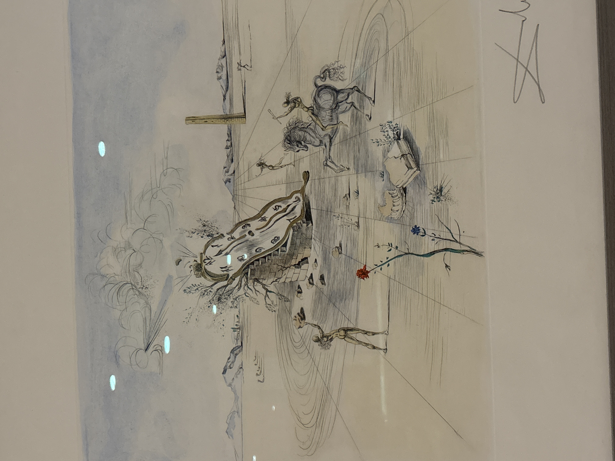 The image is a drawing, likely a print, of a surreal landscape. A large, melting clock is draped over a crumbling stone structure on the left side of the frame. A sparse, dry tree branches out from behind the clock. In the foreground, a lone, nude figure stands with their back to the viewer, holding a rock aloft. To the right of the clock, a horse and rider are depicted in motion, with the rider holding a spear or club. Further in the background, another figure appears to be running. The landscape is flat and barren, with distant mountains and a solitary, rectangular pillar in the middle ground. The sky is pale blue with wispy clouds. The overall impression is one of timelessness and decay. The artwork is signed in the lower right corner with a distinctive signature. There is no indication of the city of Dubai or the United Arab Emirates within the image itself.