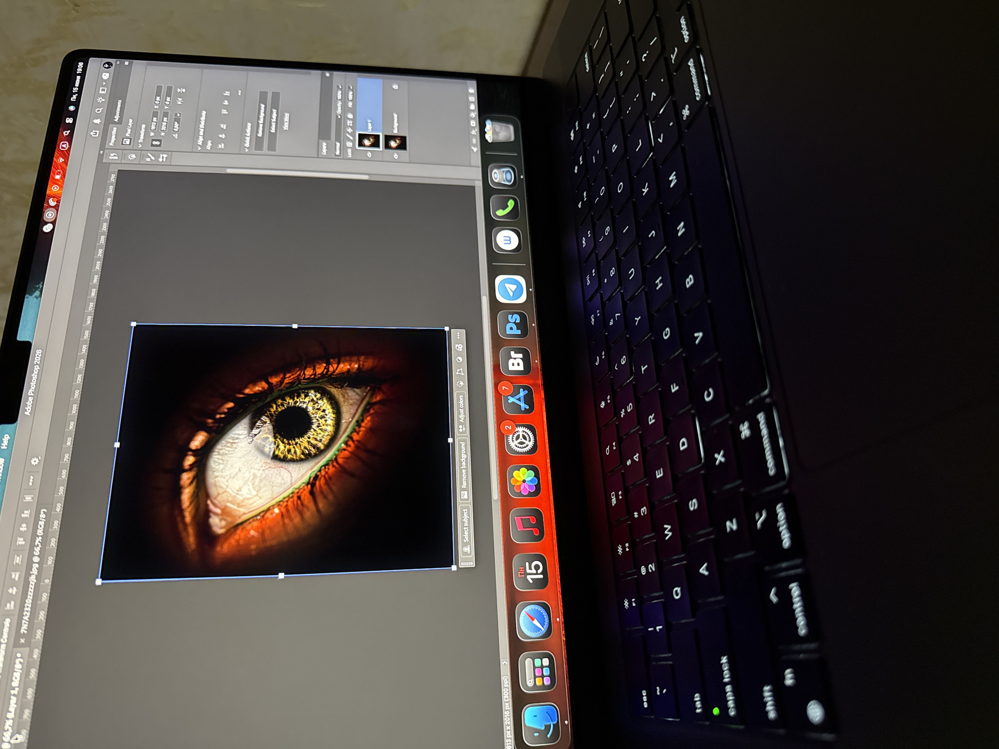 The image shows a close-up of a laptop screen displaying Adobe Photoshop with an image of a human eye. The eye is prominent, with a detailed iris and sclera, set against a dark background. The Photoshop interface is visible on the right side of the screen, showing layers and properties. The laptop is on a dark surface, with a keyboard visible in the foreground, illuminated by the screen's light. The overall scene suggests a user working on digital art or photo editing. The time stamp on the laptop screen indicates "Пн, 15 июня 19:06" which translates to "Mon, June 15, 19:06". This date format and the Cyrillic text are consistent with a location in Yerevan, Armenia.