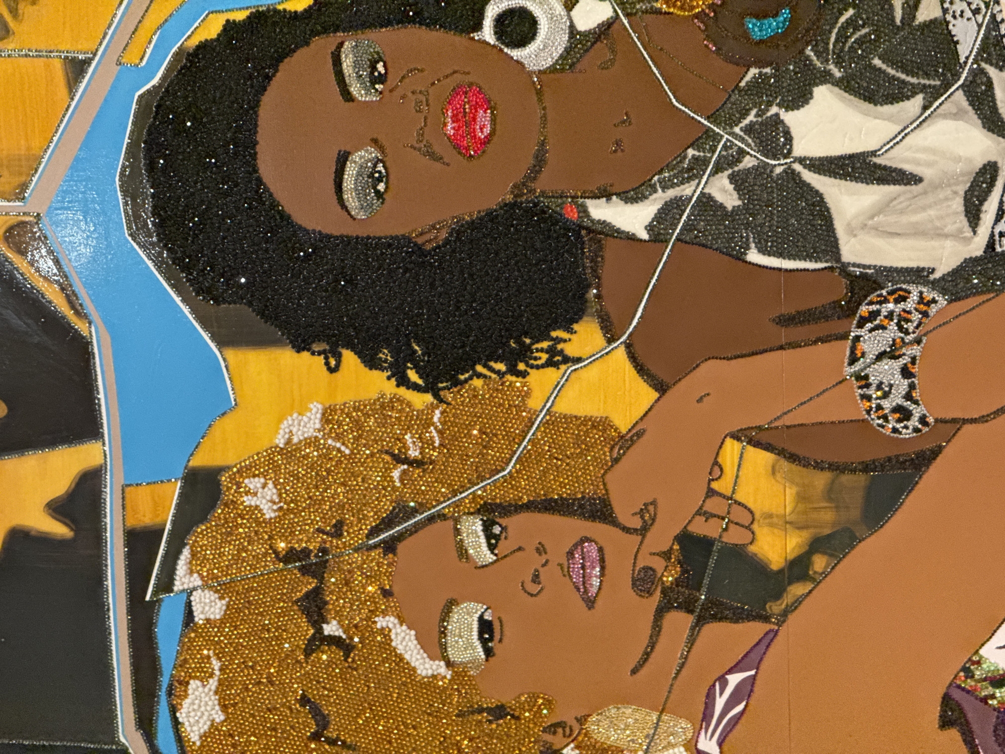 This image depicts an artwork with three figures of women, rendered in a mosaic or collage style, possibly using beads or similar materials to create texture and detail. The figures are positioned close together, their faces being the most prominent feature. The skin tones vary from lighter to darker shades of brown. The hair is stylized, with one figure having black textured hair, another having golden, beaded hair, and the third is only partially shown. The figures have decorative elements such as earrings, bracelets, and embellished clothing. The background consists of fragmented shapes in yellow, black, and blue. The overall impression is one of artistic expression, showcasing a vibrant and textured depiction of women. The image does not contain sufficient information to determine the location in San Diego, United States of America.