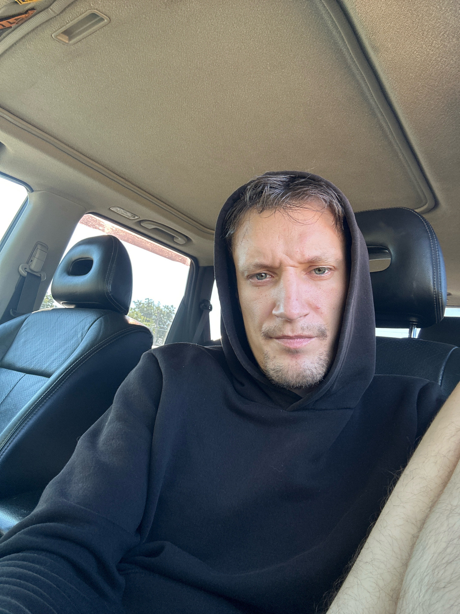The image shows a man wearing a black hoodie, sitting in the driver's seat of a car. The car's interior, including the headrest of the passenger seat and a sunroof, is visible. The man is looking directly at the camera with a serious expression. The background outside the car appears to be a sunny day with trees and foliage visible through the windows. The location of Makiv, Ukraine is not discernible from the image itself.