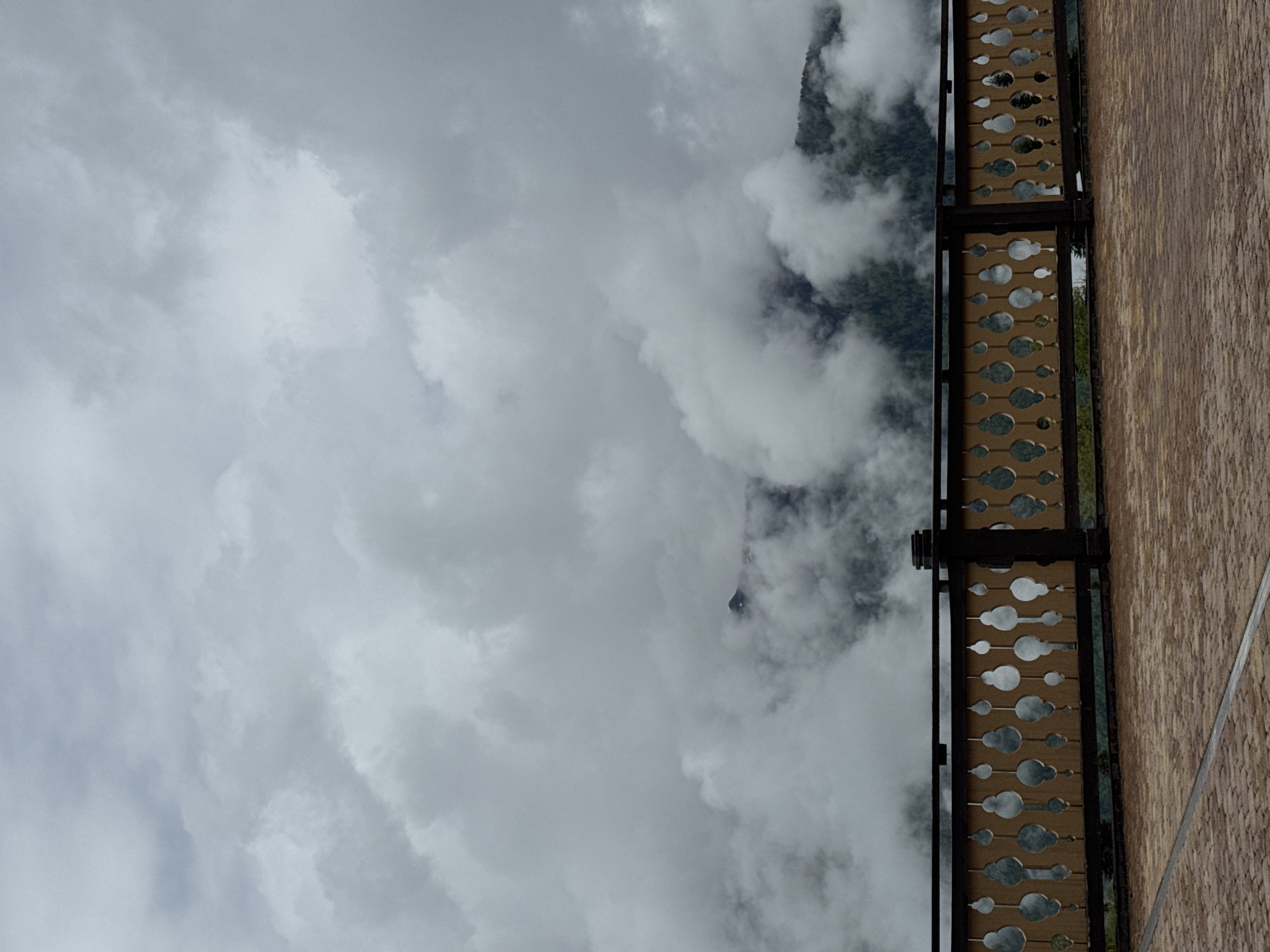View of a cloudy sky and a section of a building's balcony with decorative metal latticework in the city of Unknown, Russia. The balcony's wall is made of light brown planks.