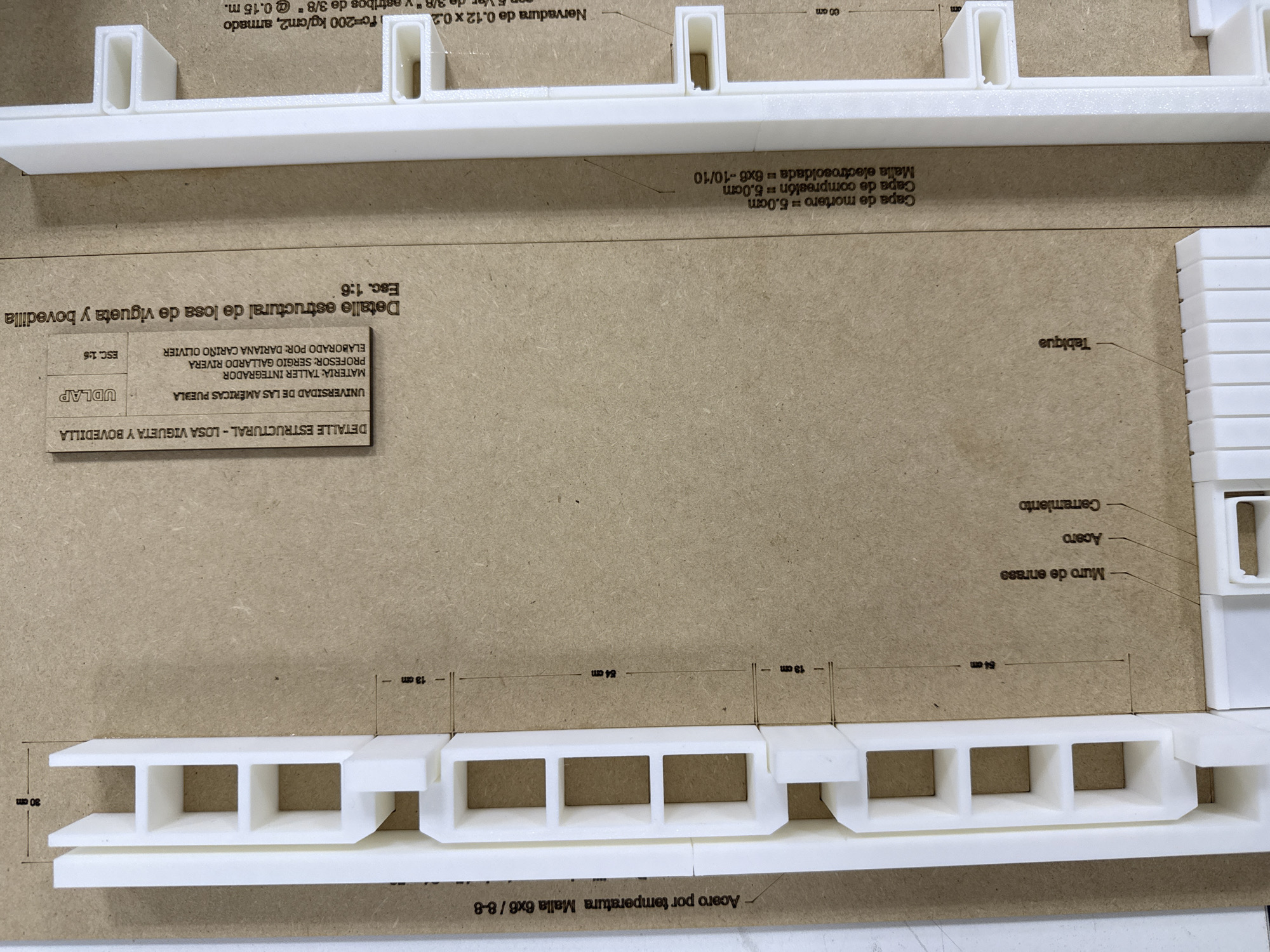 This photograph shows a detailed structural model of a rib and block slab system. The model consists of white components on a brown surface. Text labels, indicating different construction elements, are present near the model. The labels include "Muro de enrase" (Base course wall), "Acero" (Steel), "Cerramiento" (Closing), and "Tabique" (Partition). The model shows the rib, the infill blocks and the top covering with steel mesh. Dimensions are indicated in centimeters, such as "13 cm" and "54 cm". Additional text includes the names of the institution, professor, and student involved in the project, as well as a scale of "1:6". There is no information of a location or city.