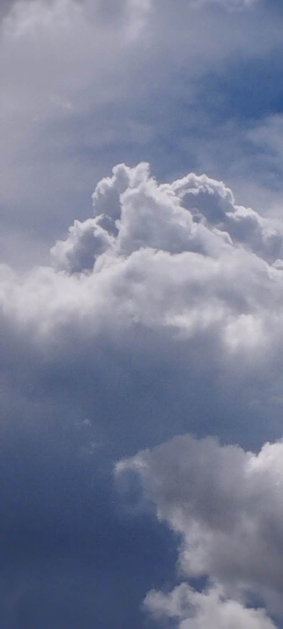 The image displays a view of the sky with clouds. There is no indication of the city of Skidzieĺ, Belarus. The clouds are predominantly white and grey, with some darker, more ominous formations towards the bottom of the frame. The lighting suggests it could be daytime, possibly with varying weather conditions. No people, objects, or actions are visible within the frame, making it a purely atmospheric scene.