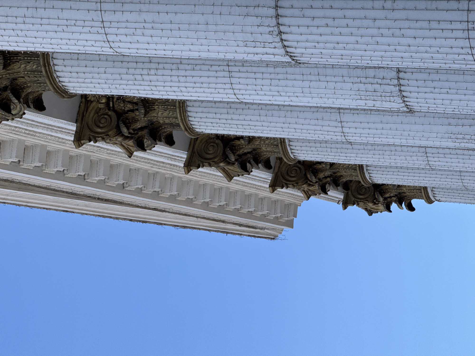 The image shows a portion of a building facade, featuring ornate architectural details. The sky is visible in the background. The facade elements are primarily white, with gold accents and classical motifs. The style suggests an older building, possibly of historical or civic significance. Location in Chita, Russia, is not definitively evident from the provided visual information.