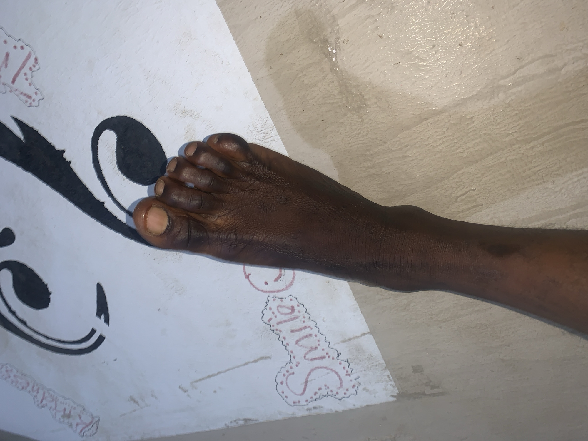 A person's bare foot, showing toes and the top of the foot, is positioned on a white surface with black abstract art. To the left of the foot, there is a drawing of a smiley face and the word "Smile" written in pink. The background appears to be a light-colored floor. The image is taken from a high angle. The location is New Stadium, Nigeria.