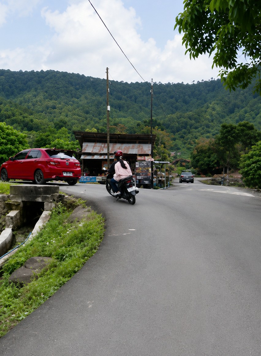 The image depicts a winding asphalt road in Turpuk Sihotang, Indonesia, bordered by lush green vegetation and a steep, tree-covered hillside under a cloudy sky. On the left side of the road, a red hatchback car is parked. Further along, a rudimentary roadside structure with a corrugated metal roof stands beside the road, displaying various items for sale. A man and a woman are riding a scooter, heading away from the viewer. The woman, wearing a pink shirt and a helmet, is driving, while the man, also wearing a helmet, is the passenger. A black car is visible further down the road, approaching from the opposite direction. The overall scene suggests a rural or semi-rural setting in Indonesia.